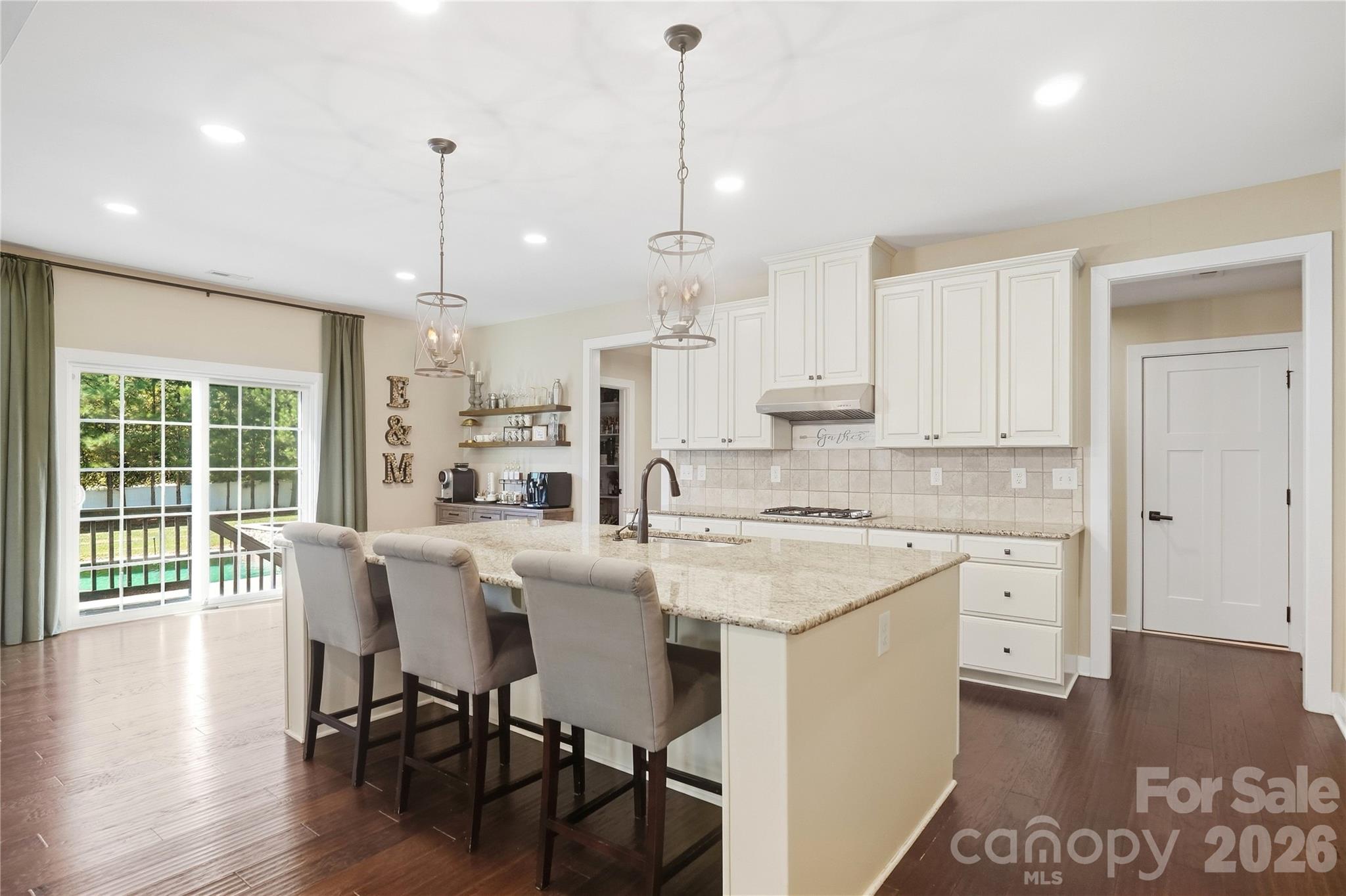 Kitchen with a large granite island with seating, pendant lighting, abundant cabinetry, a gas cooktop, and a walk-in pantry with wood shelving. - 912 Manorwood Drive, Waxhaw
