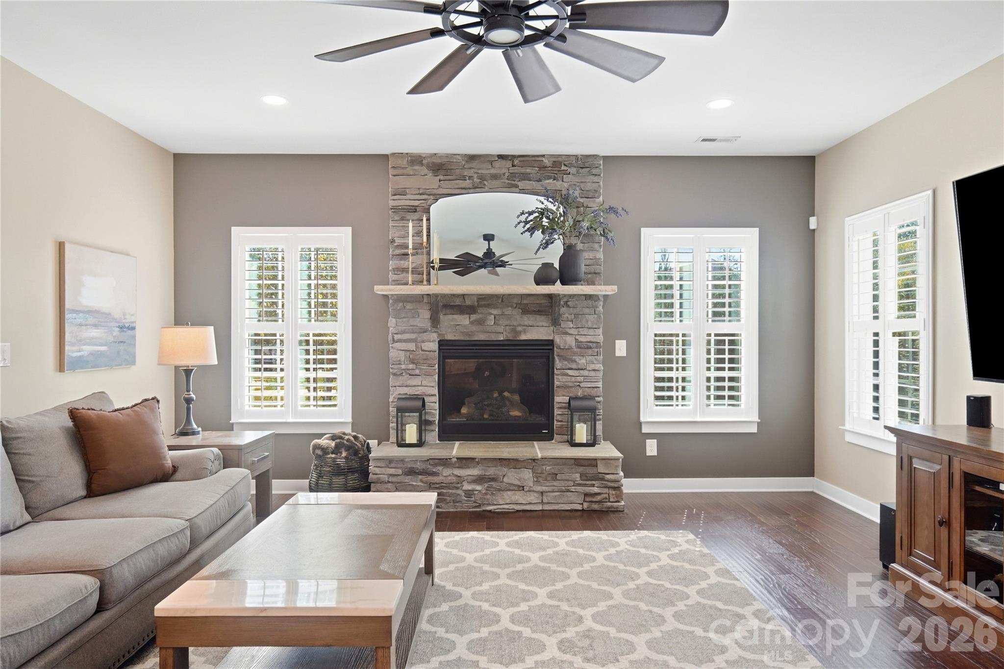 Stone gas fireplace with a raised hearth and mantel, flanked by plantation-shuttered windows. - 912 Manorwood Drive, Waxhaw