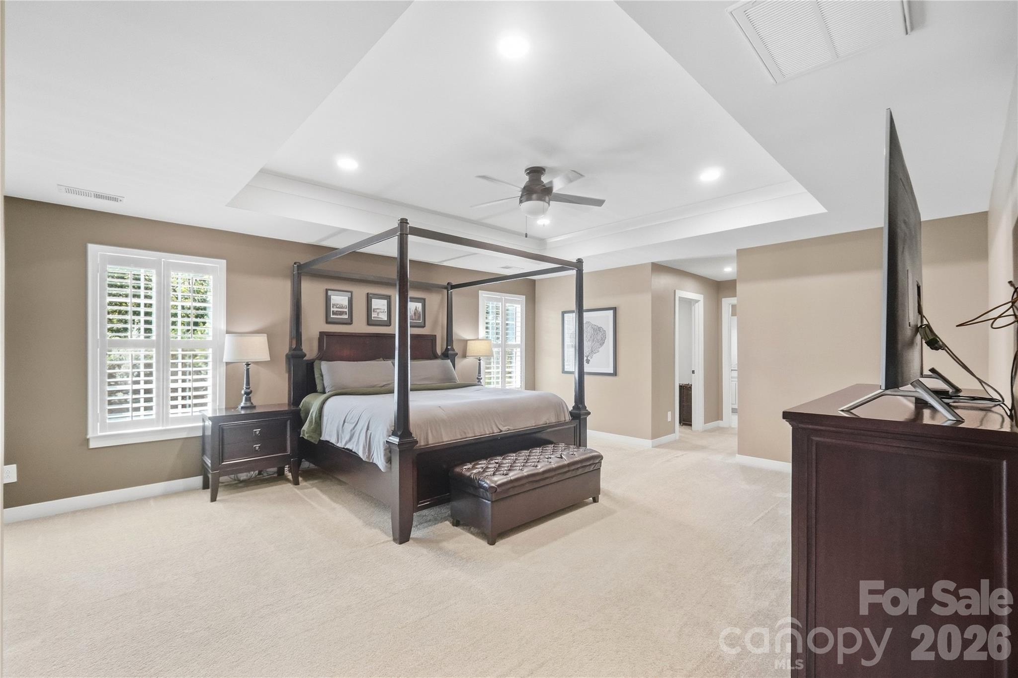 Spacious primary bedroom with a tray ceiling, ceiling fan, recessed lighting, and plantation shutters. - 912 Manorwood Drive, Waxhaw
