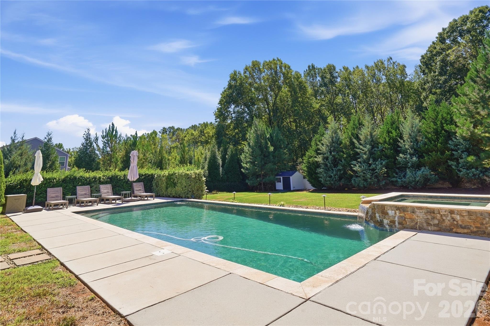 Heated 16x34 saltwater pool with a raised spa and spillover waterfall, stone coping, and landscape lighting. - 912 Manorwood Drive, Waxhaw