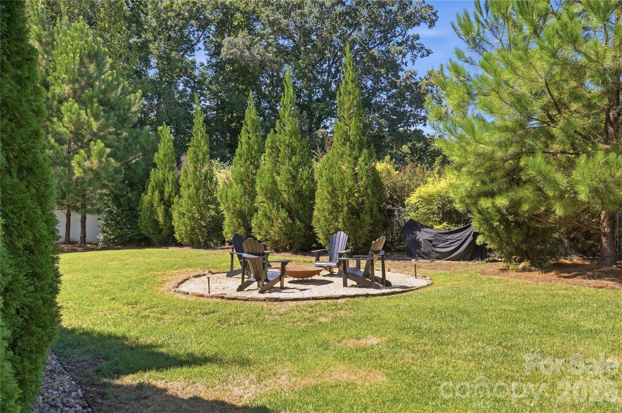 Gathering area with a fire pit, set among evergreens in the backyard. - 912 Manorwood Drive, Waxhaw