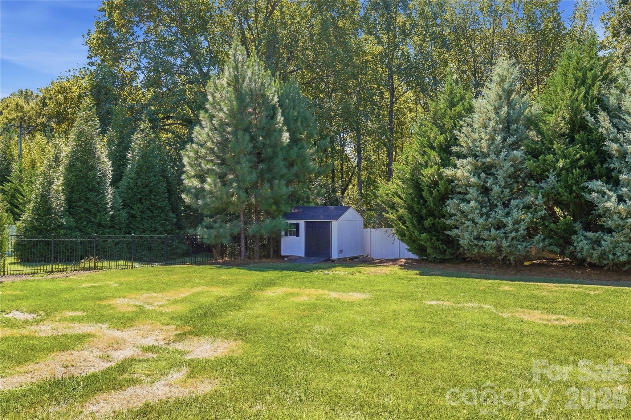 Backyard storage shed tucked among mature trees. The shed, a zero-turn mower, and an aerator all convey. - 912 Manorwood Drive, Waxhaw