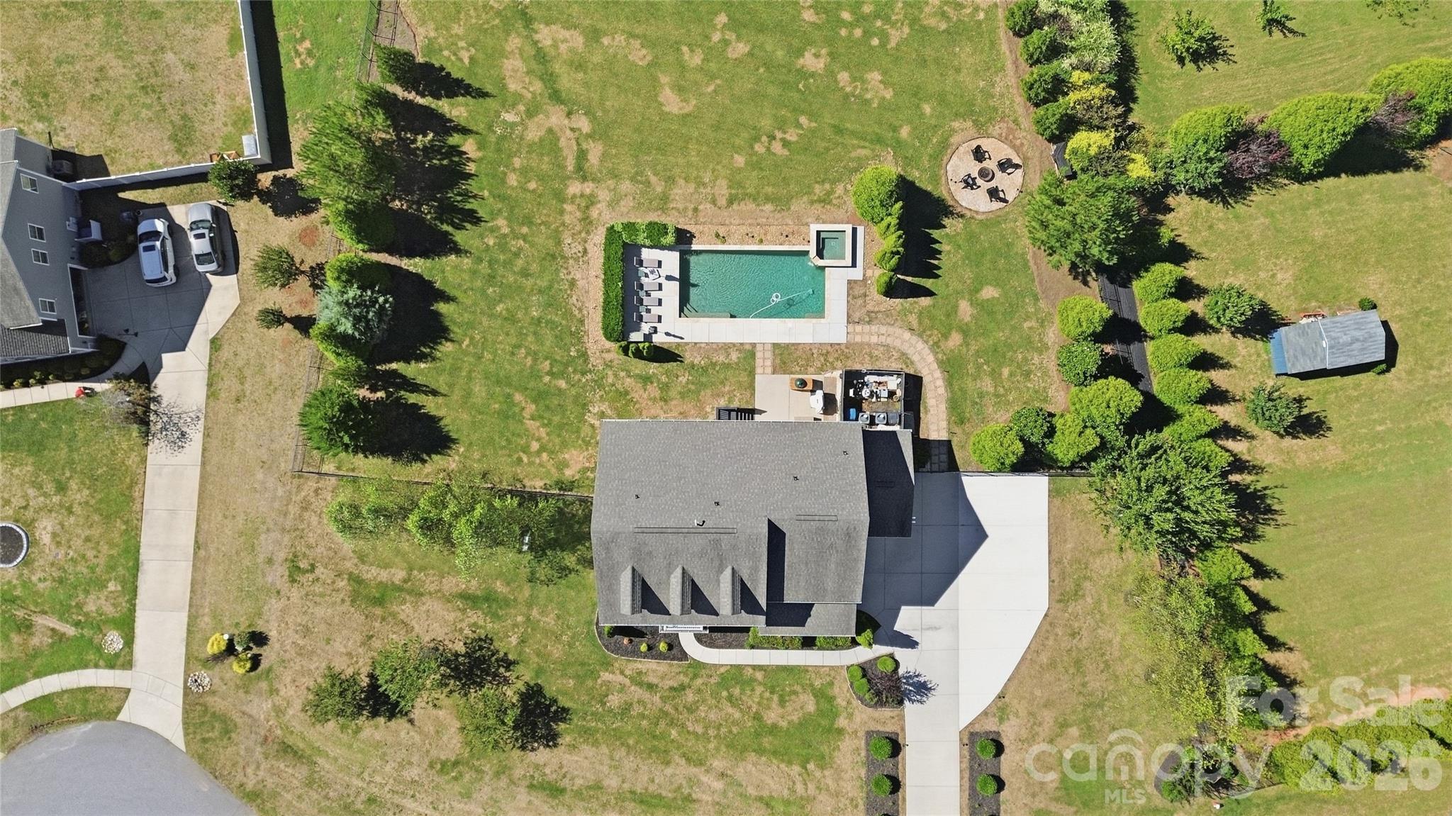 Overhead view of the 0.94-acre property: a fully fenced backyard with the heated saltwater pool and spa, a fire pit, a storage shed, and generous open lawn, lined with mature evergreens. - 912 Manorwood Drive, Waxhaw