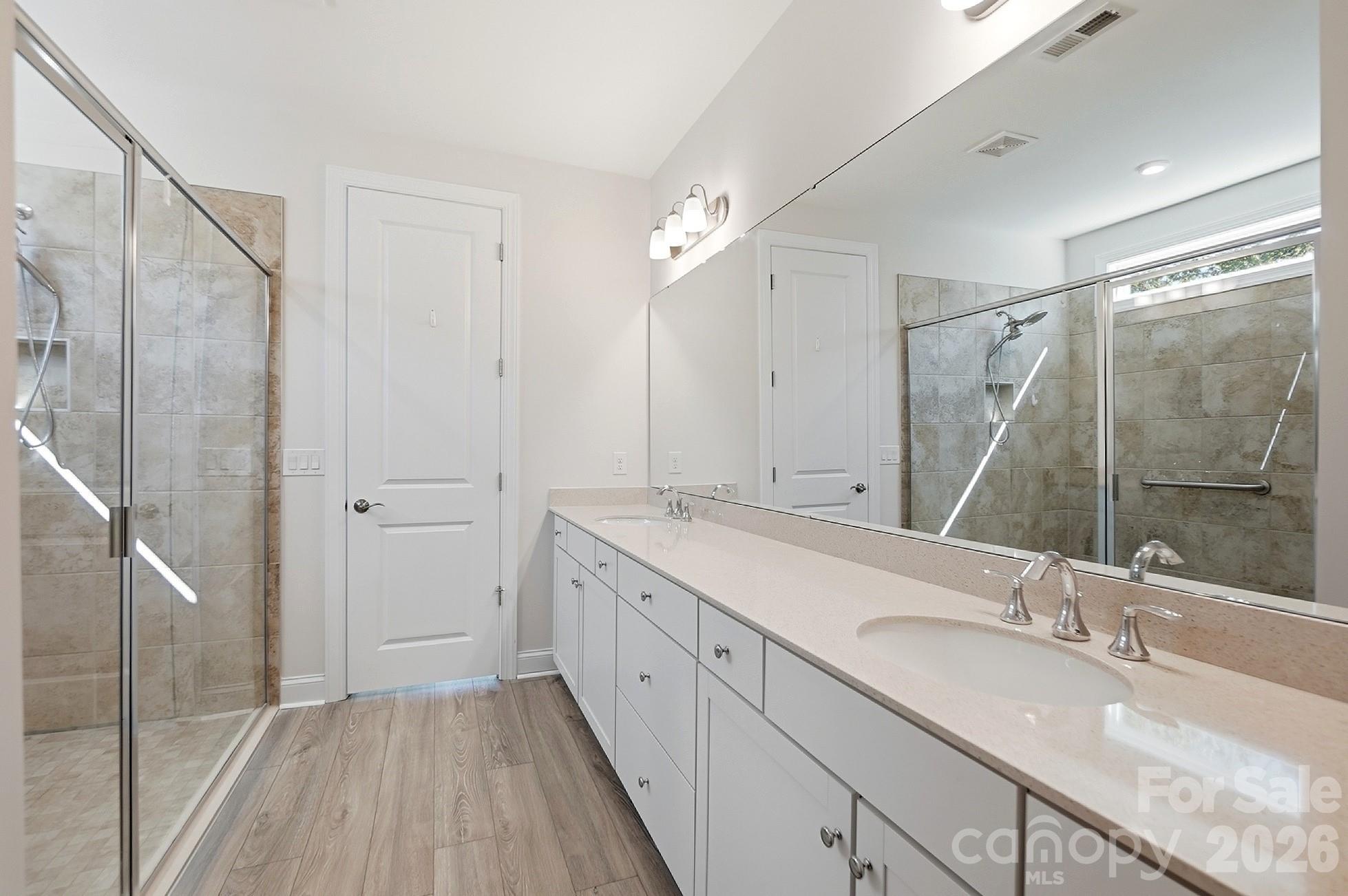 Luxurious primary bath offers dual vanities, an oversized walk-in tile shower with handicap grab bar, and a large walk-in closet - 8032 Longwaters Court, York