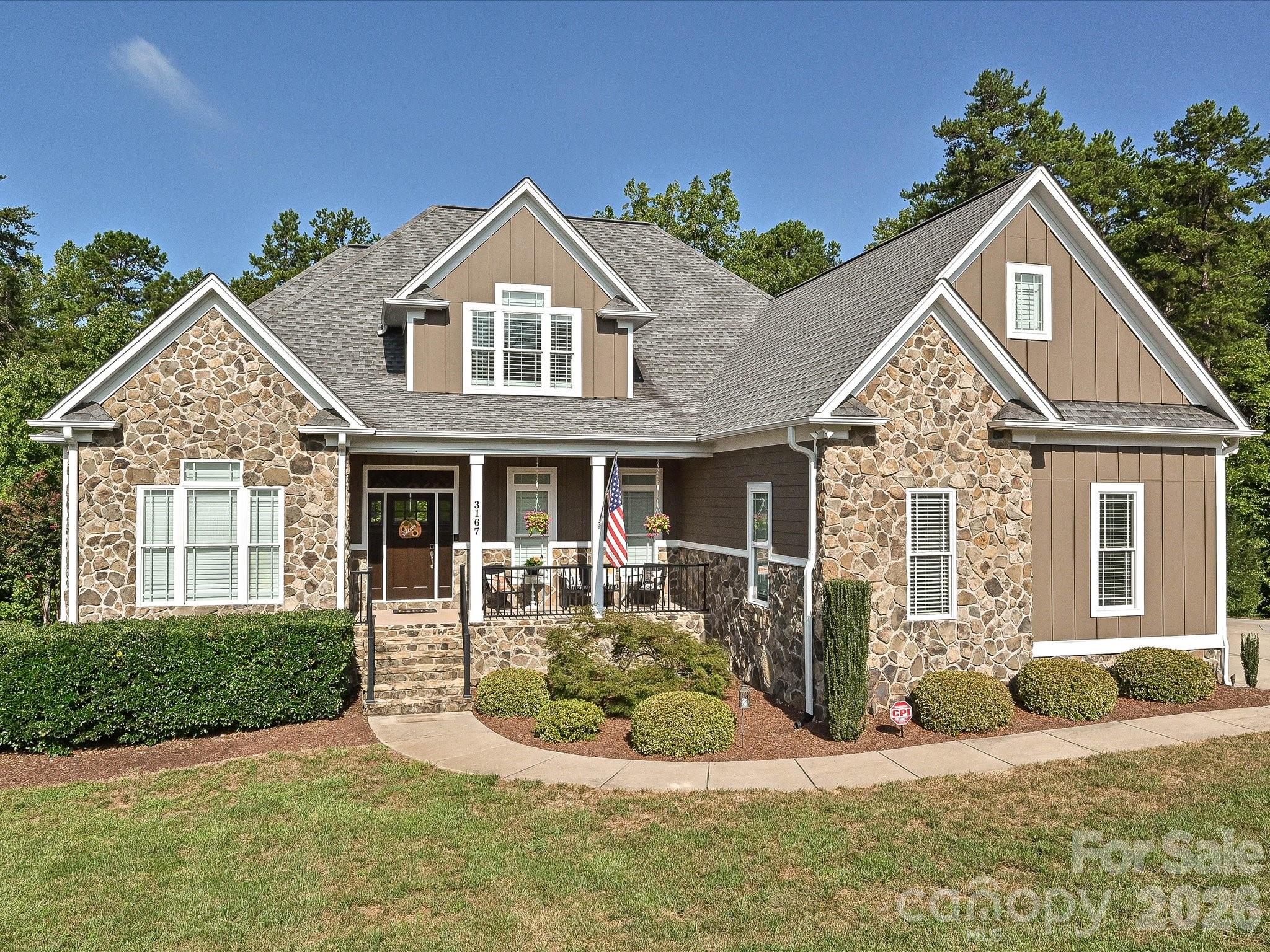 A striking stone-and-siding exterior showcases timeless architecture, a welcoming covered front porch, beautifully maintained landscaping, and impressive curb appeal. - 3167 James Plantation Drive, Denver