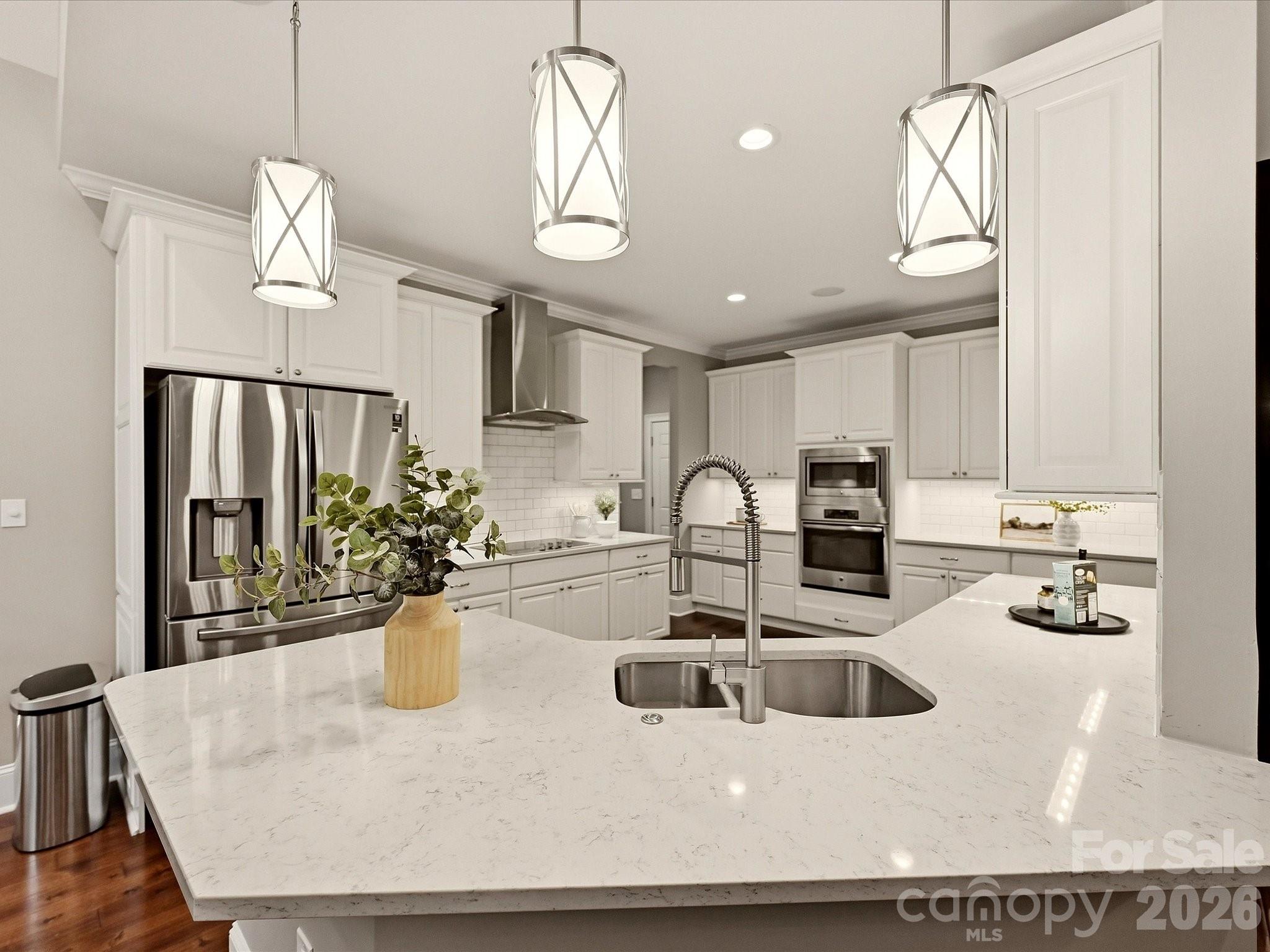 A bright, beautifully appointed kitchen features crisp white cabinetry, quartz countertops, stainless steel appliances, stylish pendant lighting, and an expansive island for workspace or seating. - 3167 James Plantation Drive, Denver