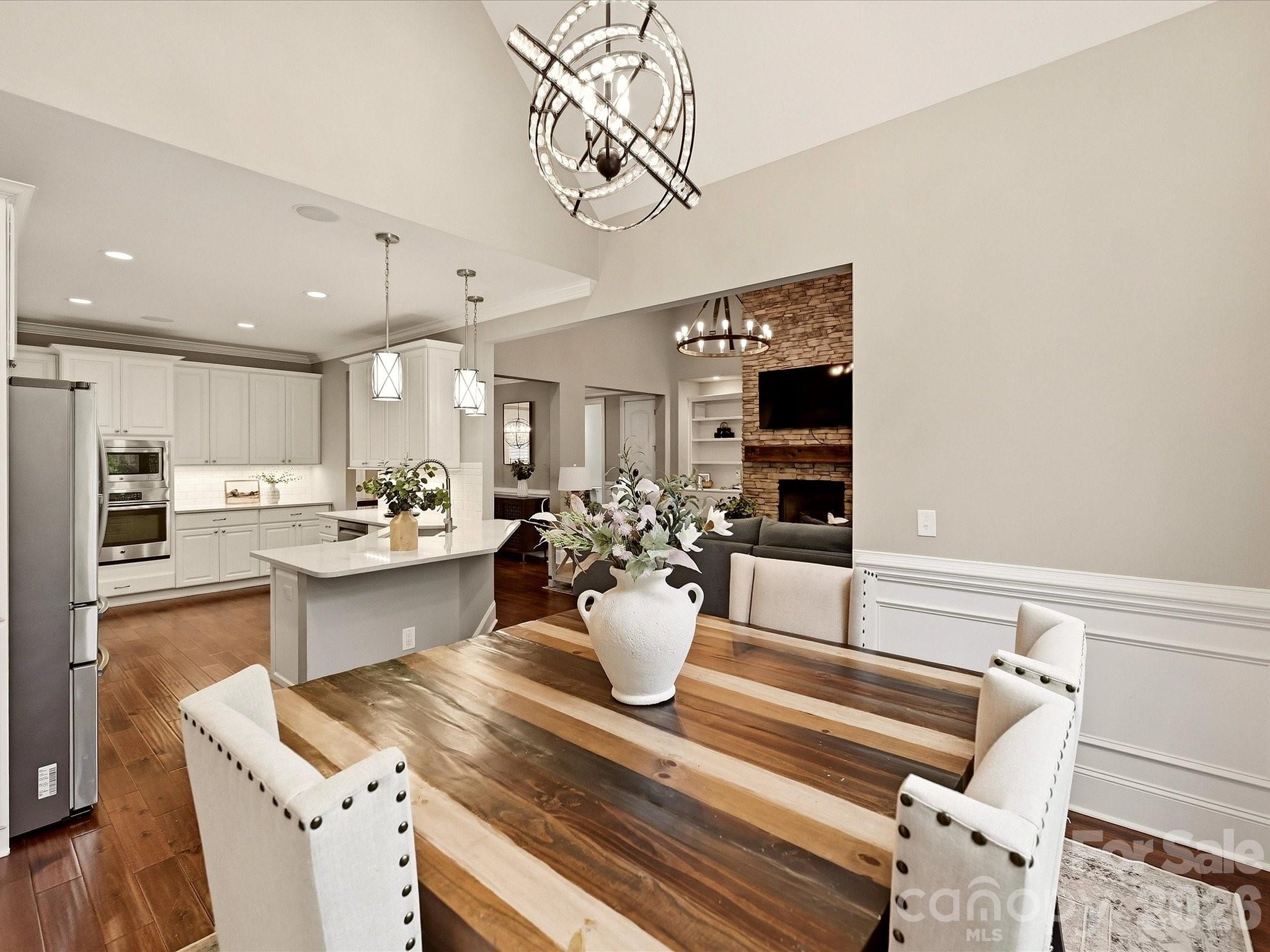 A light-filled breakfast/dining area features vaulted ceilings, hardwood floors, elegant wainscoting, a statement chandelier, and expansive windows overlooking the surrounding greenery. - 3167 James Plantation Drive, Denver