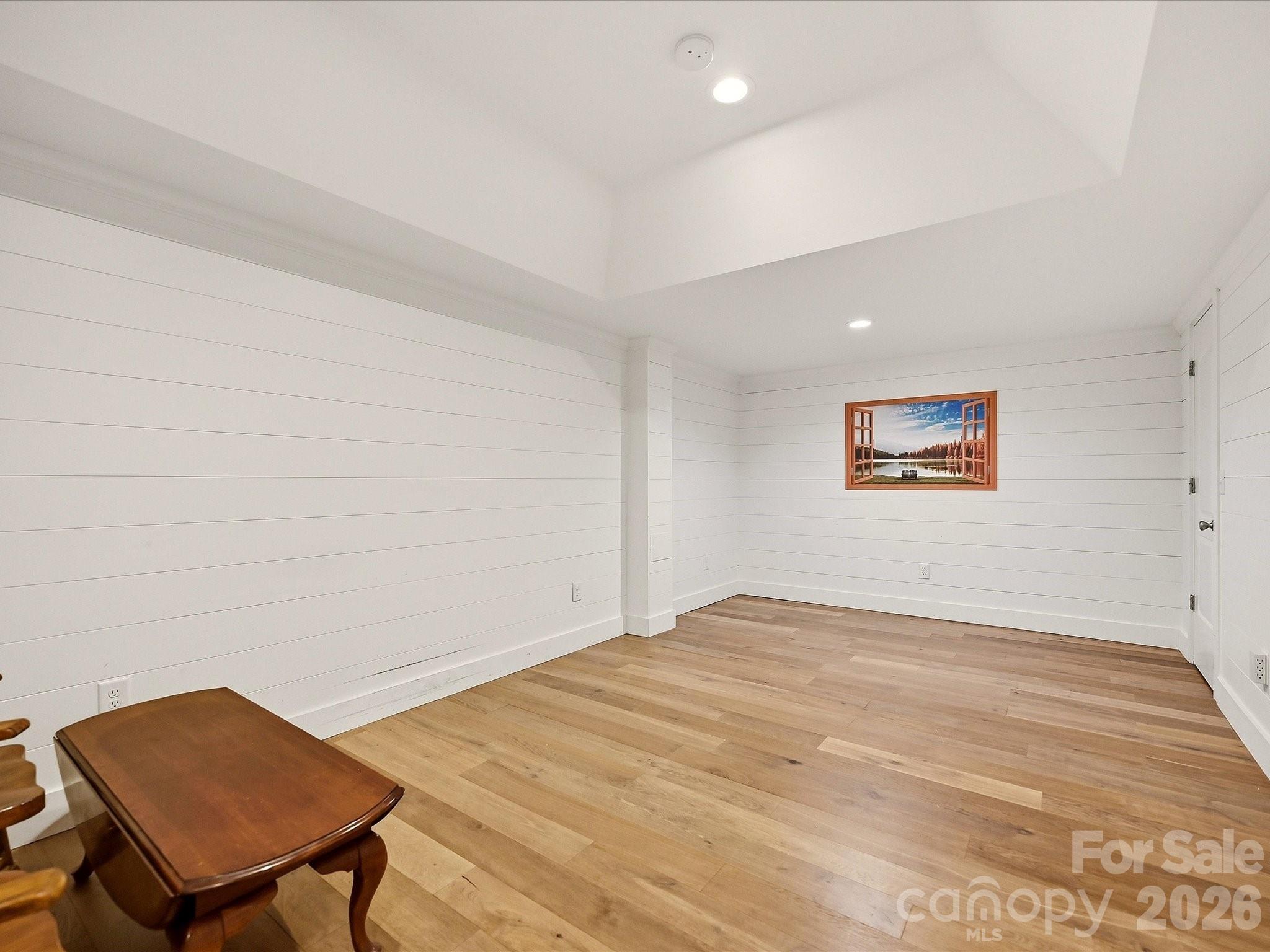 A spacious flex room features light wood flooring, tray ceiling, shiplap walls, recessed lighting, and ample space for a home office, media room, playroom, or additional living area. - 3167 James Plantation Drive, Denver