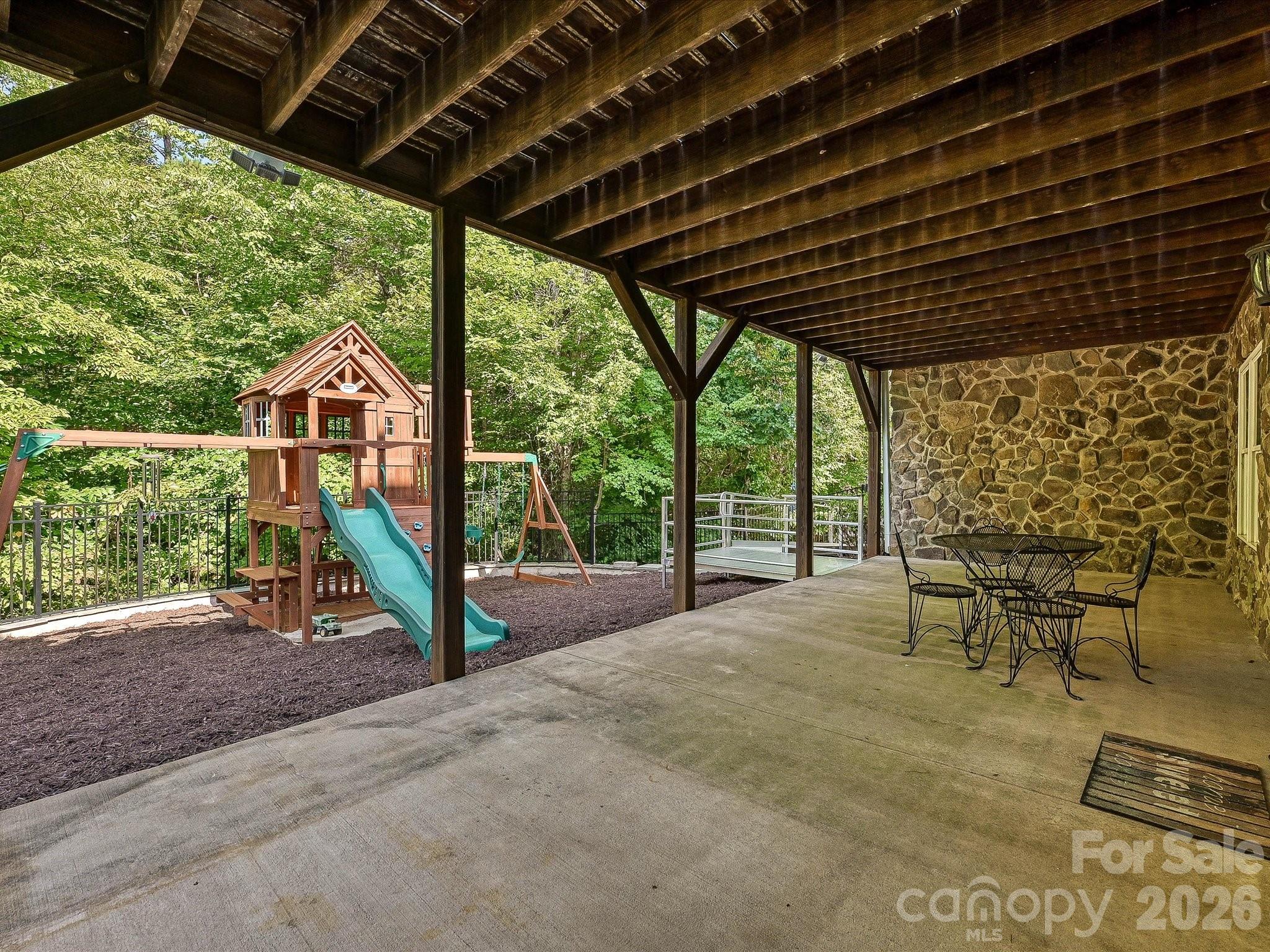 A spacious covered patio with exposed wood beams and stone accents provides a shaded outdoor retreat overlooking the fenced, tree-lined backyard and play area. - 3167 James Plantation Drive, Denver