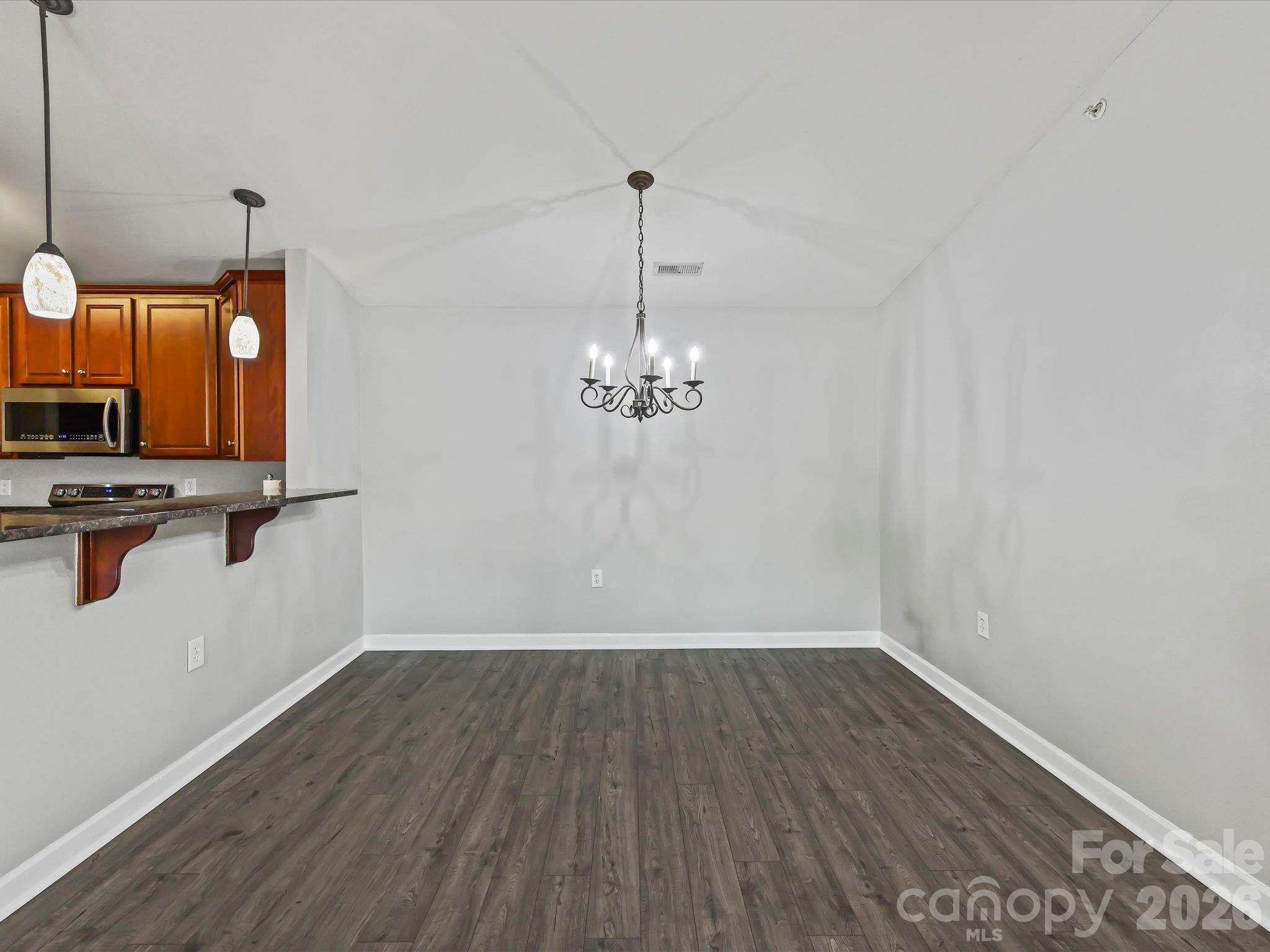 Spacious dining area featuring LVP flooring, a vaulted ceiling, decorative chandelier, and a convenient breakfast bar connecting seamlessly to the kitchen. - 9031 Mcdowell Creek Court, Cornelius