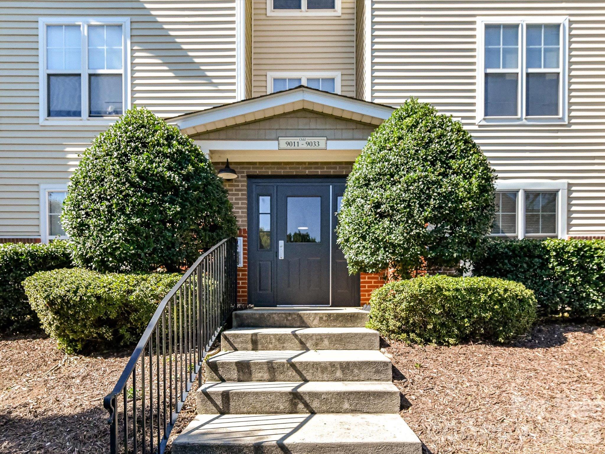 Welcoming building entrance featuring attractive landscaping, a covered entry, and convenient stair access to the main doors. - 9031 Mcdowell Creek Court, Cornelius