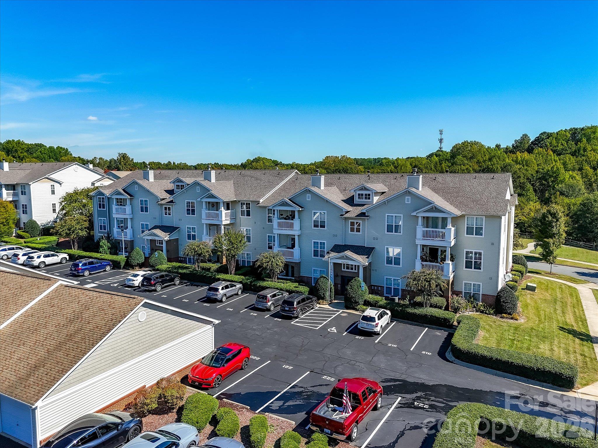 Aerial drone view showcases the well-maintained condo building, convenient parking, mature landscaping, and attractive community setting. - 9031 Mcdowell Creek Court, Cornelius