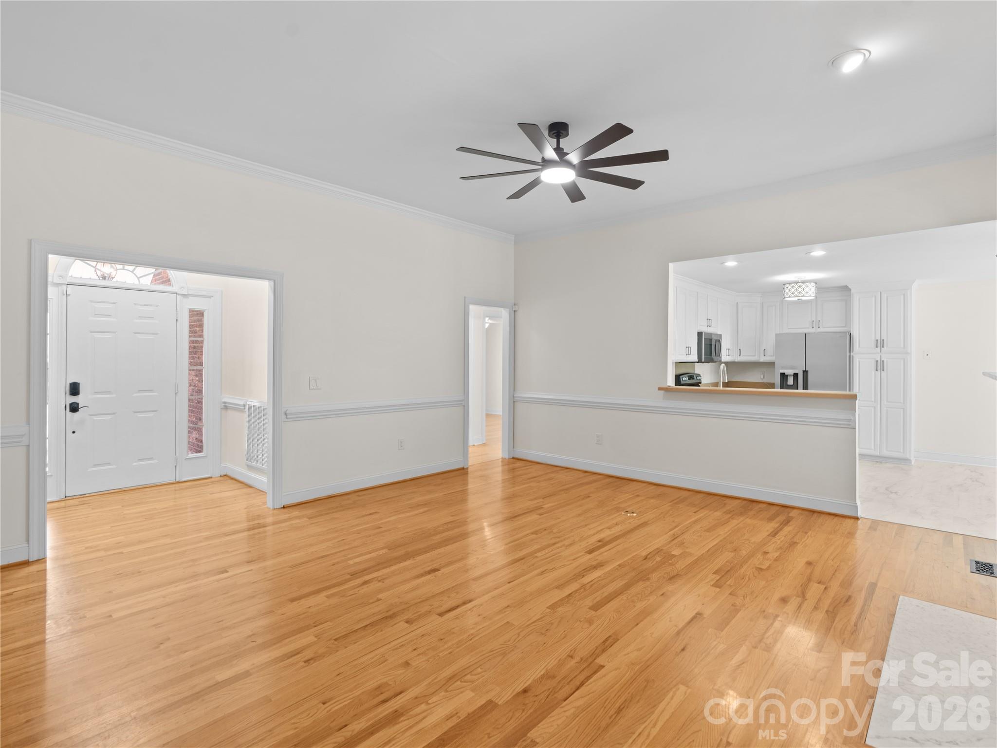 Bright and spacious living room featuring gleaming hardwood floors, crisp chair rail molding, a modern ceiling fan, and the pass-through towards the kitchen. - 1011 Overhill Road, Salisbury