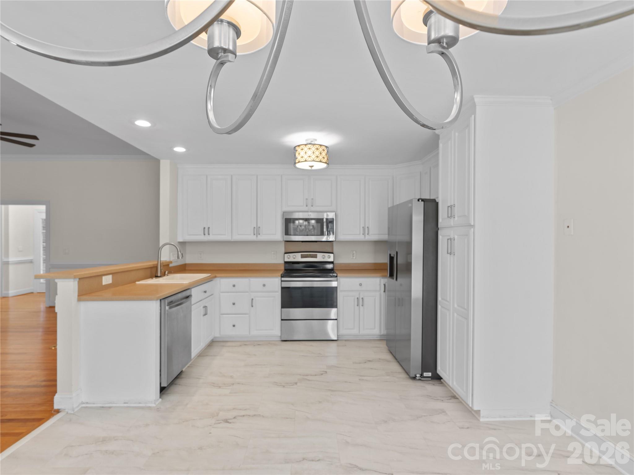 Bright, modern kitchen featuring crisp white cabinetry, stainless steel appliances, marble-look LVP flooring, built-in pantry storage, and a raised breakfast bar overlooking the living area. - 1011 Overhill Road, Salisbury