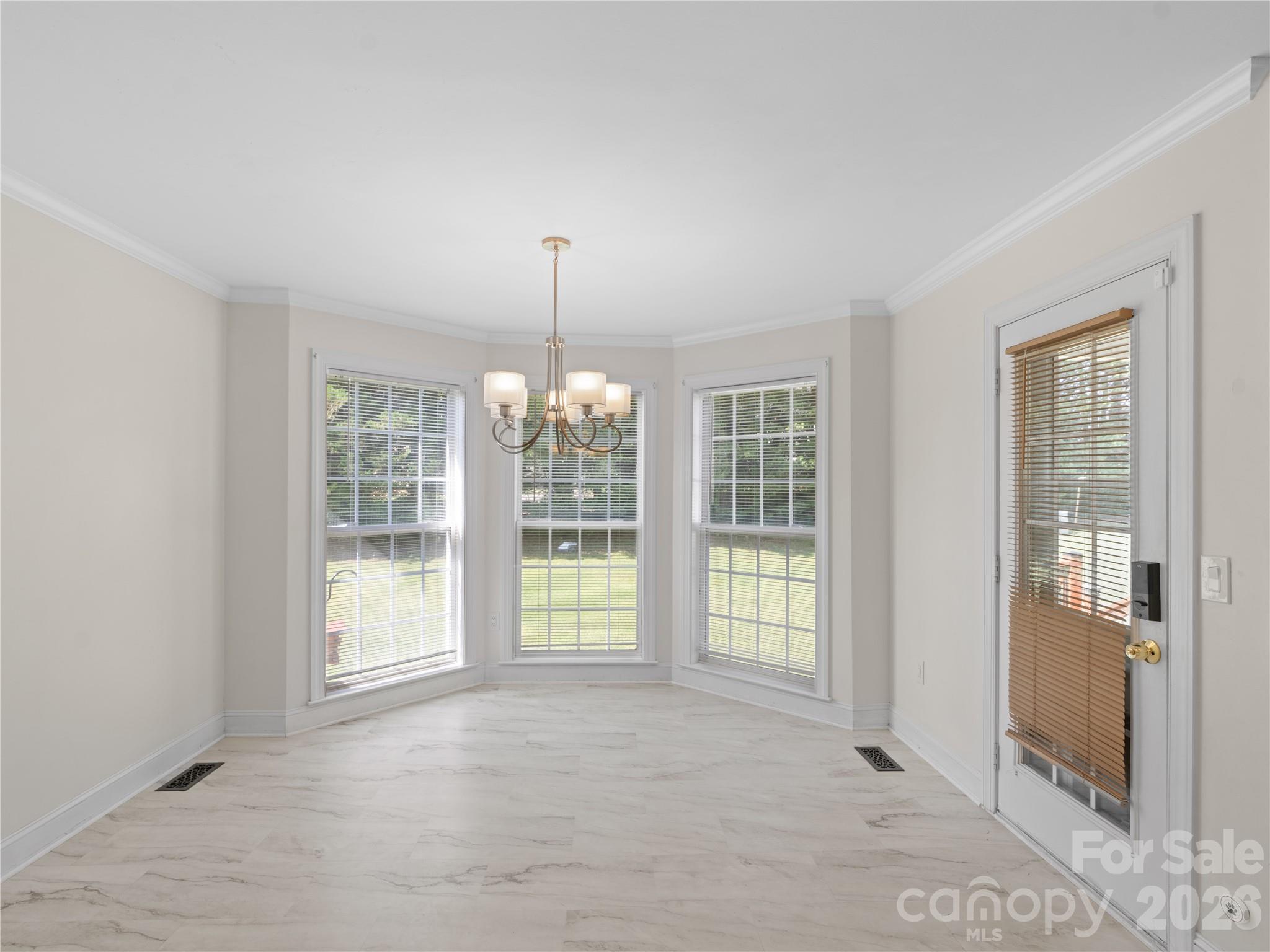Sunlit breakfast nook featuring a classic bay window, stylish chandelier fixture, crisp crown molding, marble-look flooring, and direct access door to the back deck and a motion detected doggie door. - 1011 Overhill Road, Salisbury