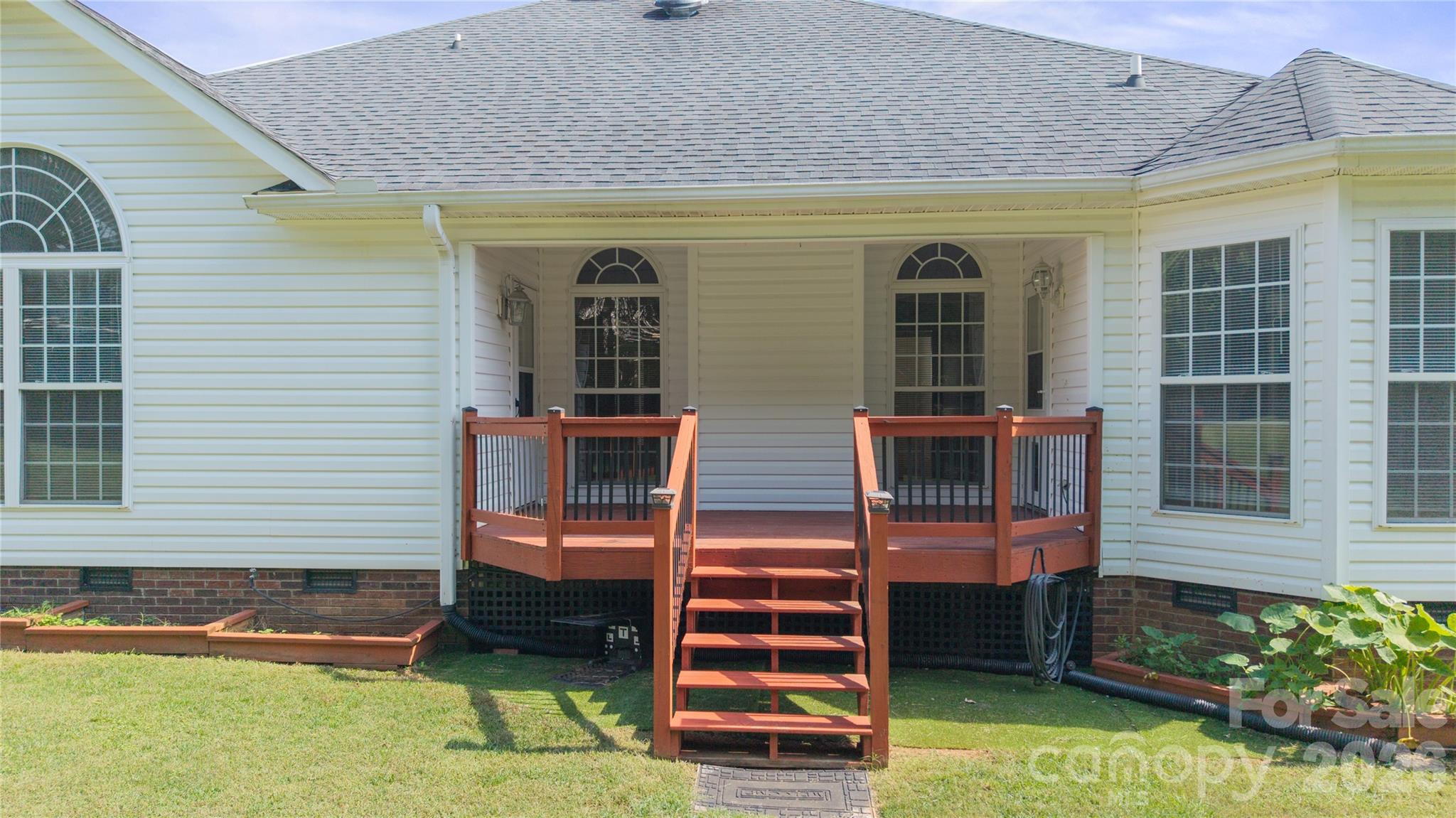 Inviting covered back deck with stained wooden railings, centered steps down to the lawn, and direct access doors through to the kitchen on the right and primary suite on the left. - 1011 Overhill Road, Salisbury