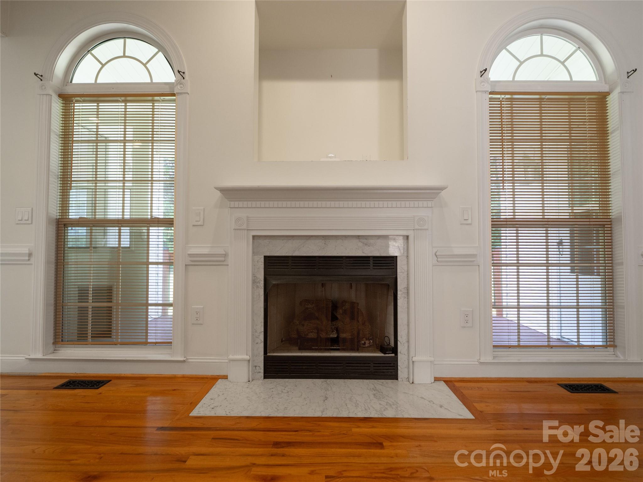 Living room focal point featuring a fireplace with marble surround, white mantle, built-in media nook above, and flanking tall arched windows letting in abundant natural light. Just outside the windows is the covered back deck. - 1011 Overhill Road, Salisbury