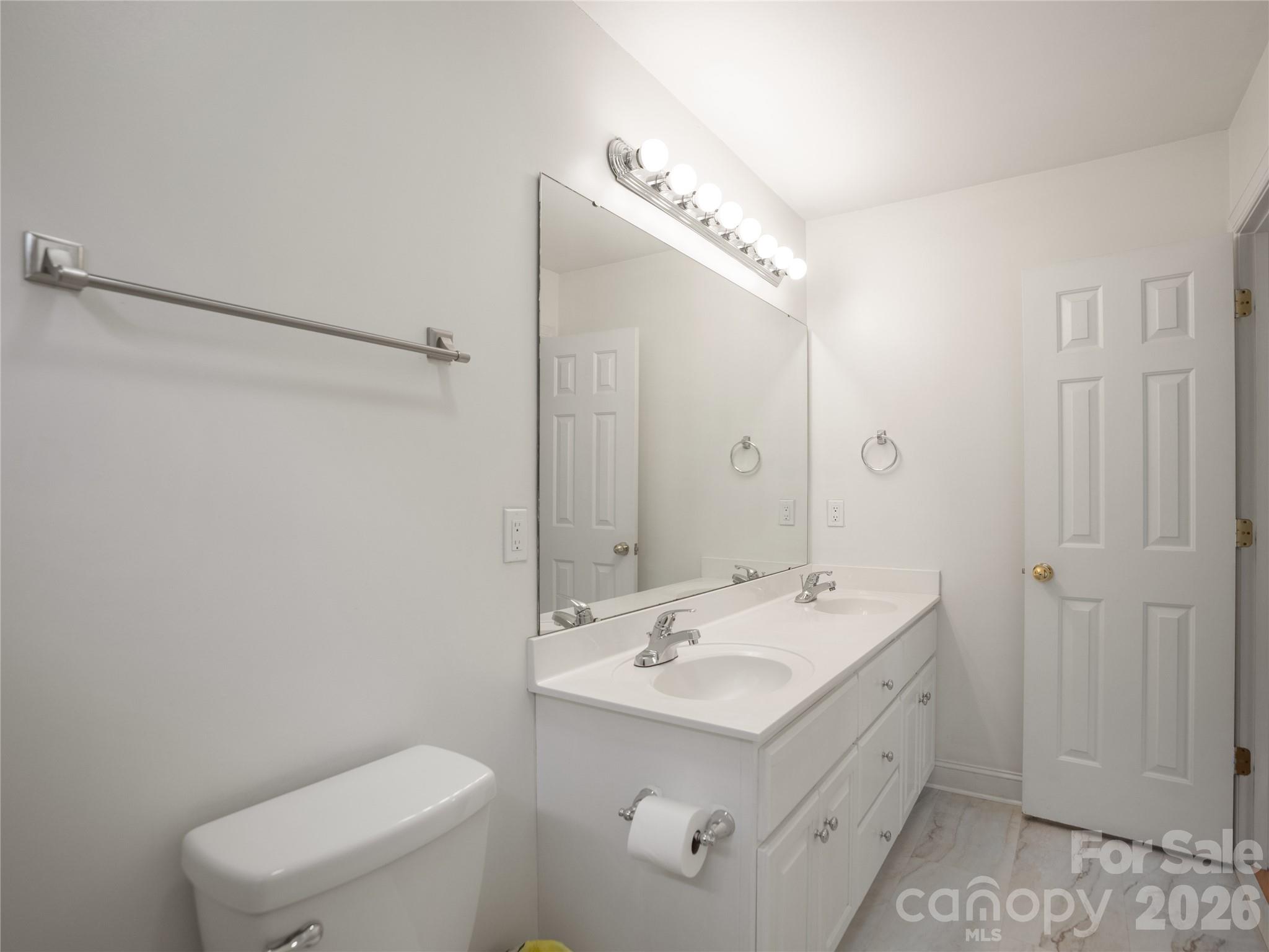 Bright secondary bathroom featuring a dual-sink vanity, expansive vanity mirror with multi-bulb lighting, white cabinetry, and updated flooring. - 1011 Overhill Road, Salisbury