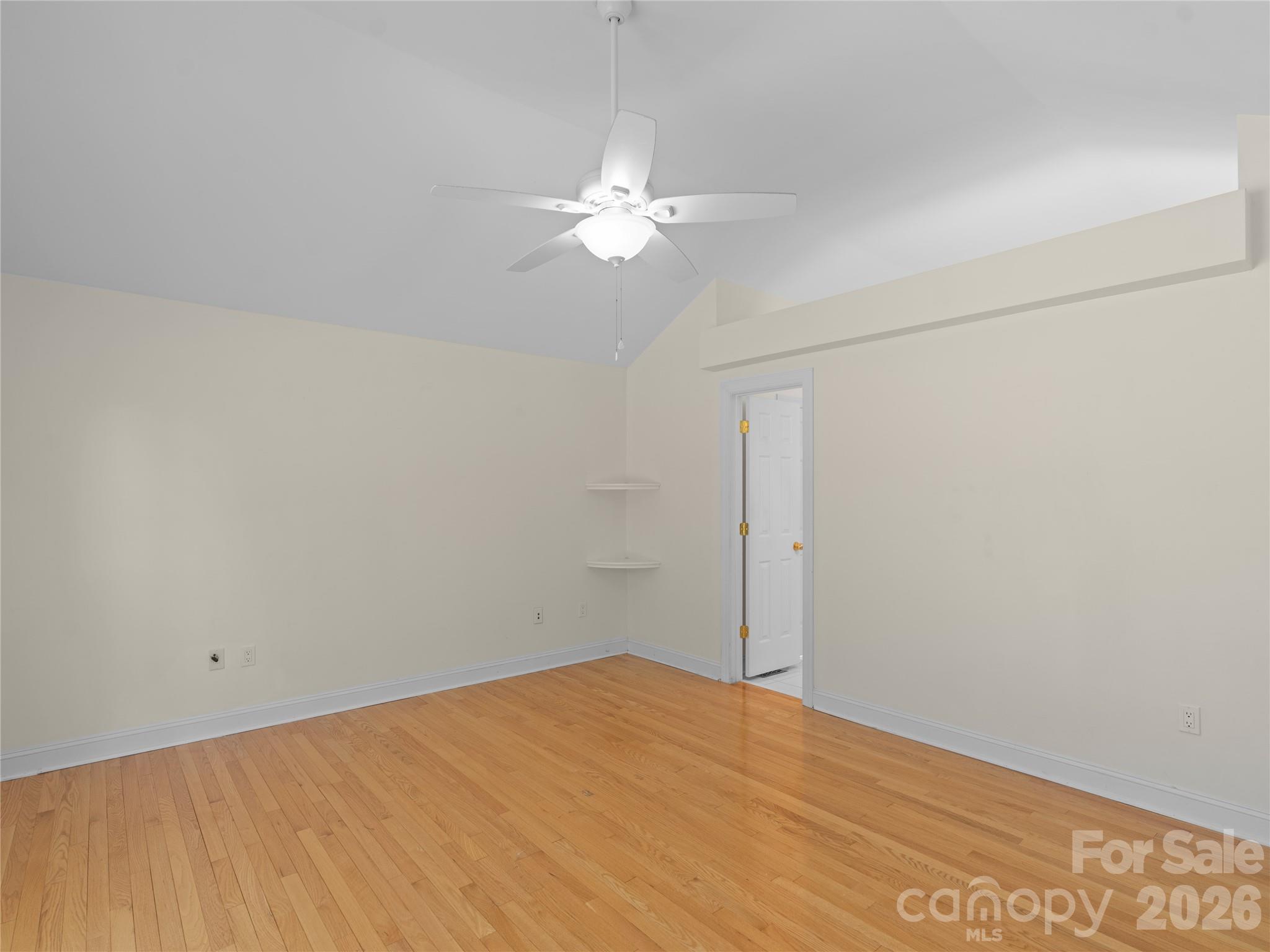 Spacious primary suite featuring soaring vaulted ceilings, warm hardwood flooring, a modern ceiling fan, high display ledge or plant shelf and an open doorway leading seamlessly into the ensuite bath. - 1011 Overhill Road, Salisbury