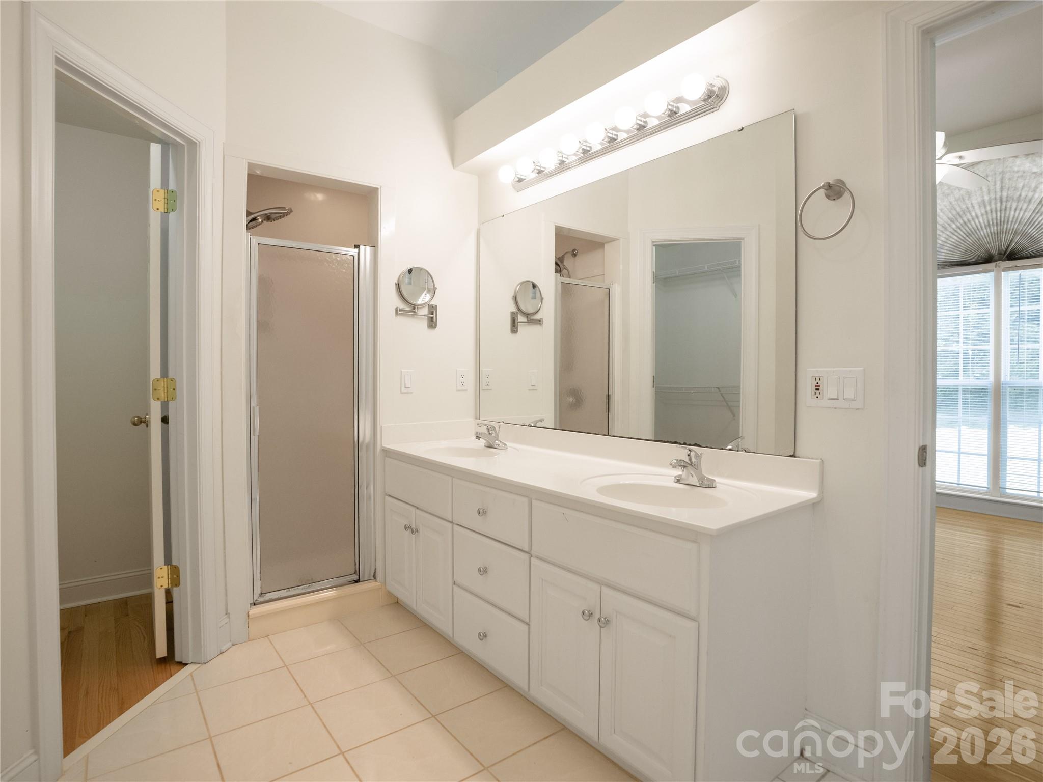 Primary suite vanity area showcasing a dual-sink vanity with abundant cabinetry, framed walk-in shower, large wall mirror, tile flooring, and direct access to dual walk-in closets - 1011 Overhill Road, Salisbury