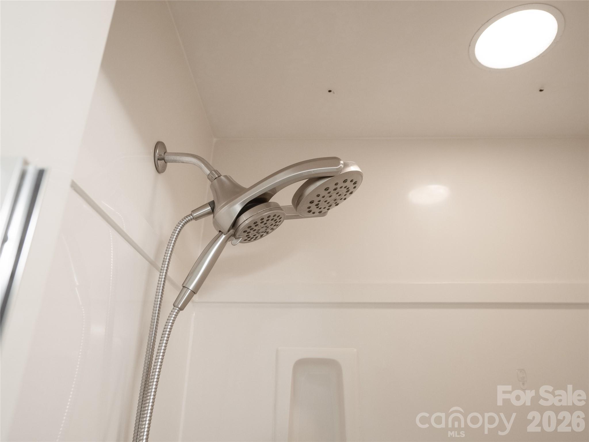 Close-up detail of the updated dual shower head system featuring a fixed overhead spray head and a flexible detachable handheld sprayer in brushed nickel finish. - 1011 Overhill Road, Salisbury