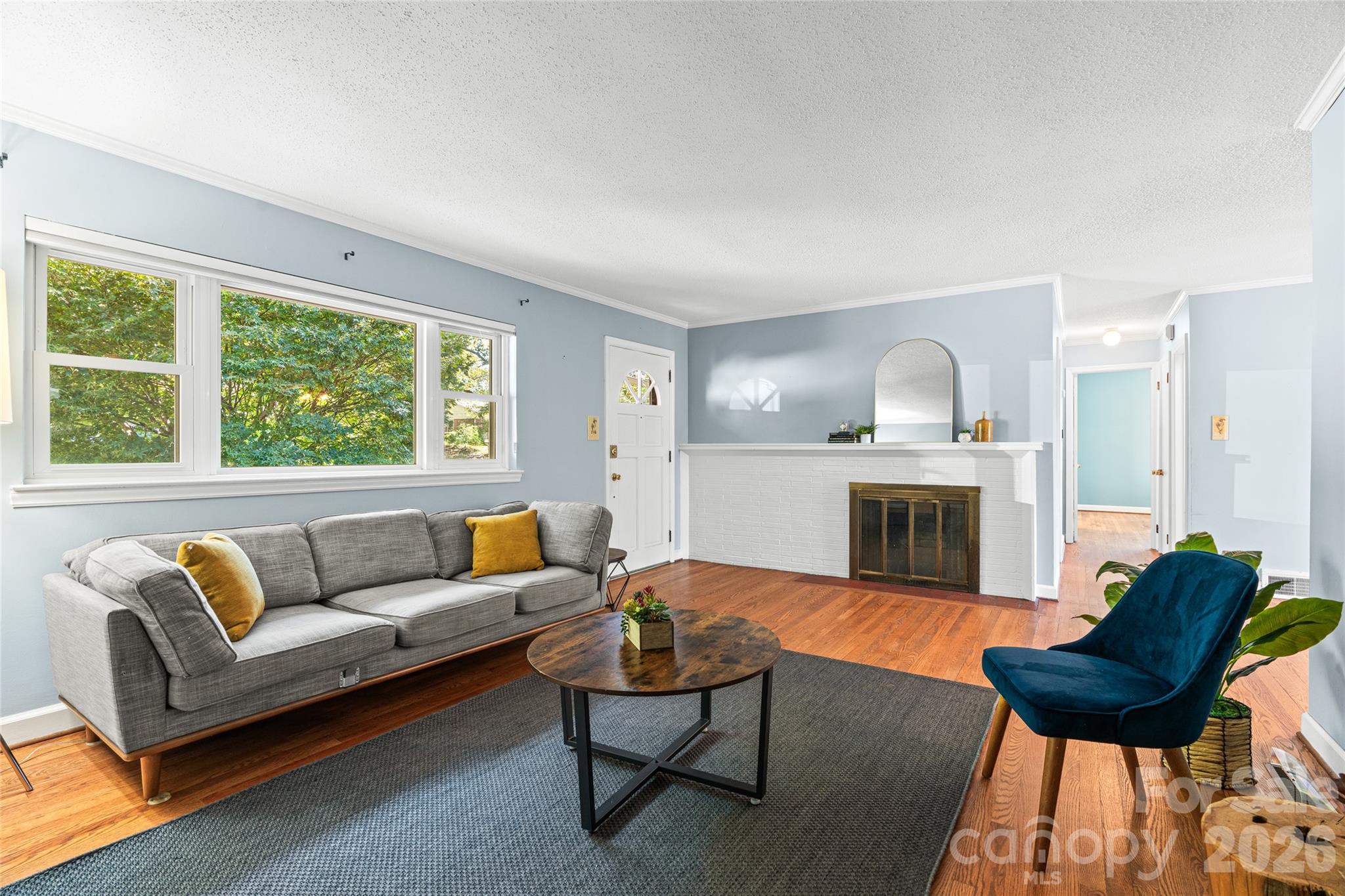 Light-filled living room featuring large windows, hardwood floors, and a classic brick fireplace and mantel. - 18 Northwood Road, Asheville