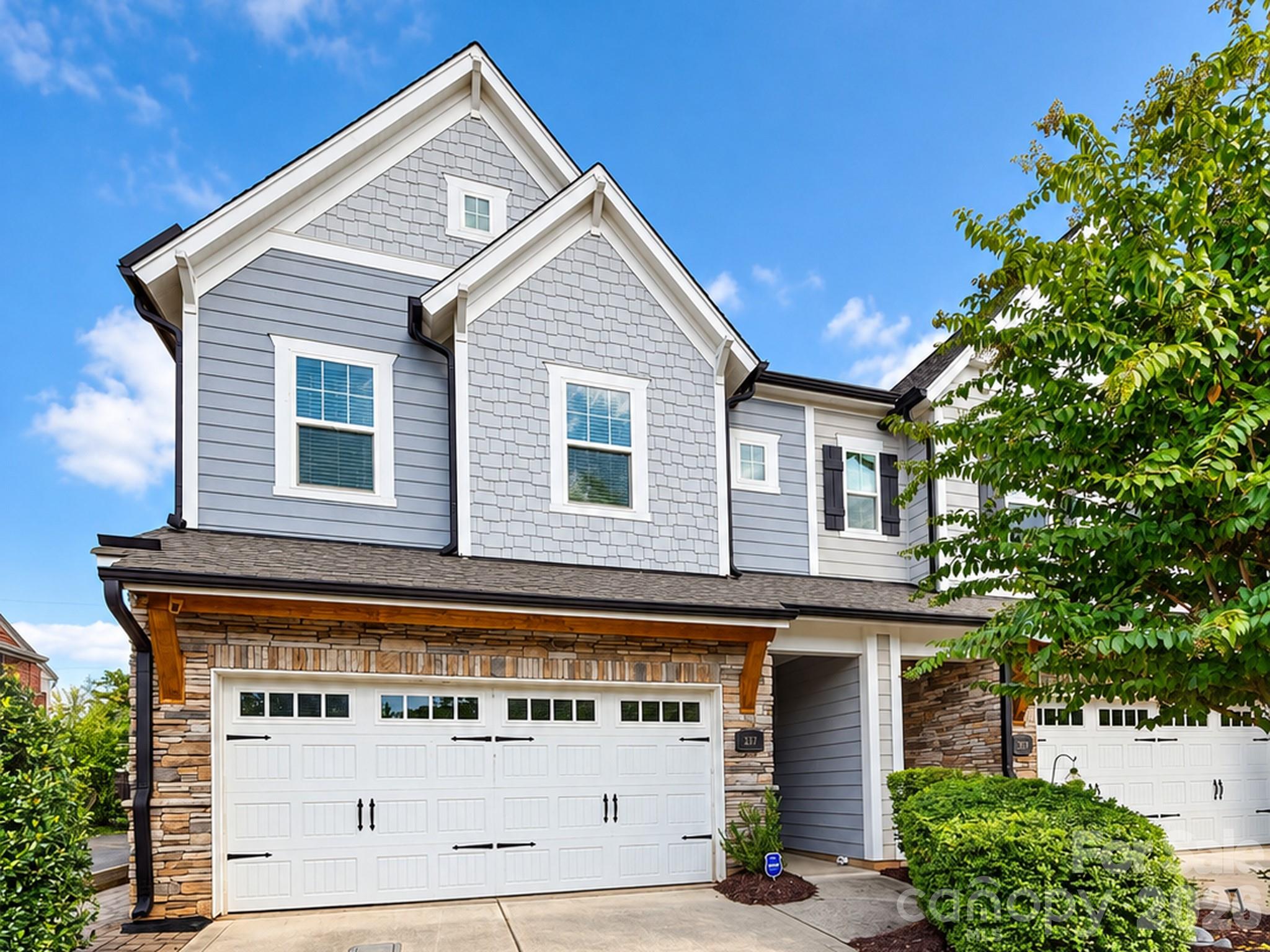 Front exterior of 337 Belton St, a 2019 end-unit townhome in Charlotte, NC 28209 near South End. Craftsman-inspired facade with shake siding, stacked stone accents, carriage-style two-car garage door, and mature landscaping. - 337 Belton Street, Charlotte