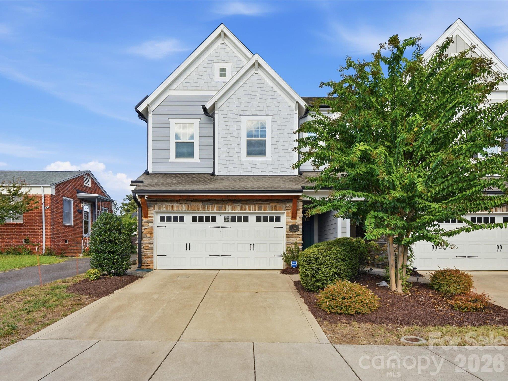 Curb appeal at this South End Charlotte end-unit townhome: wide concrete driveway, attached two-car garage, stone and shake exterior, and mature landscaping in a walkable 28209 location. - 337 Belton Street, Charlotte