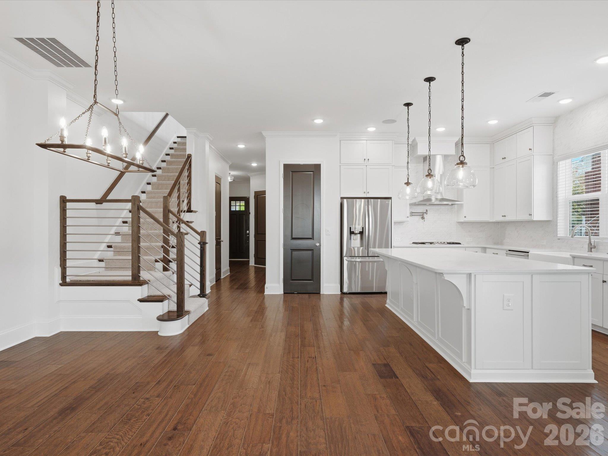 Open floor plan connecting the dining area, white chef's kitchen with oversized island, and modern staircase with horizontal metal railing. Ideal layout for entertaining. - 337 Belton Street, Charlotte