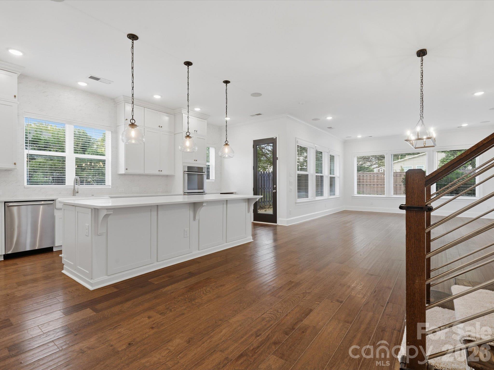 Designer kitchen with custom white shaker cabinetry, oversized center island with glass pendant lighting, stainless steel appliances, double wall ovens, and LVP floors flowing into the living area. - 337 Belton Street, Charlotte