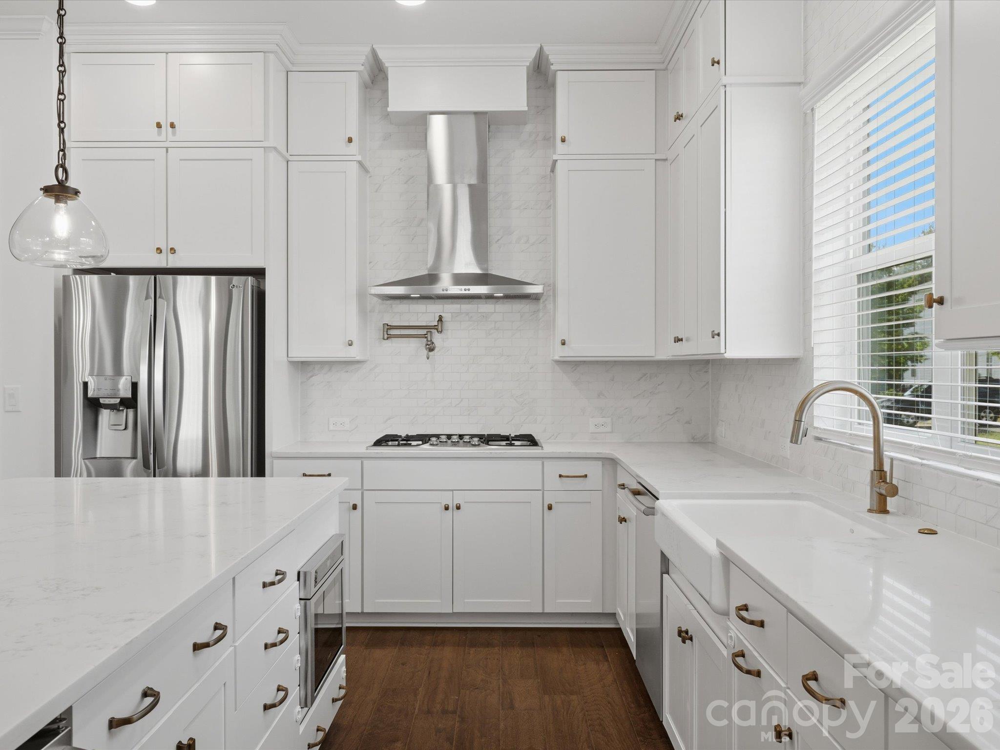 Chef's kitchen detail: gas cooktop with stainless chimney hood, pot filler, marble-look subway tile backsplash, farmhouse apron-front sink, gold faucet and hardware, and stainless French-door refrigerator. - 337 Belton Street, Charlotte