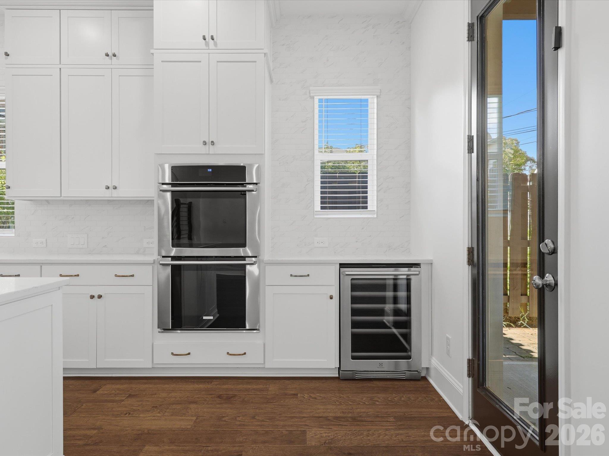 Kitchen wall with built-in stainless double ovens, a second wine refrigerator, and glass door to the covered rear patio and fenced backyard. Dual wine fridges for entertaining. - 337 Belton Street, Charlotte