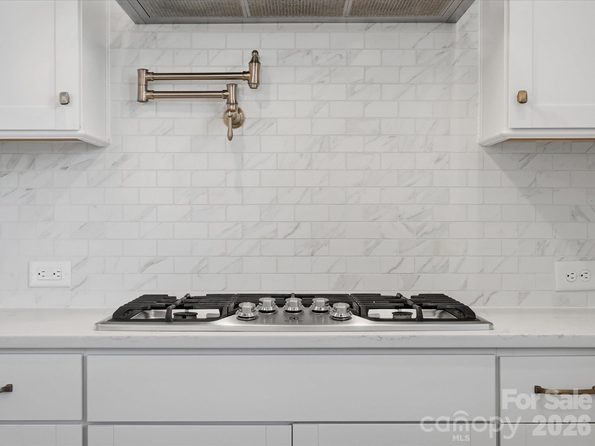 Luxury kitchen detail: wall-mounted pot filler above a stainless gas cooktop, marble-look subway tile backsplash, and custom white shaker cabinetry. - 337 Belton Street, Charlotte