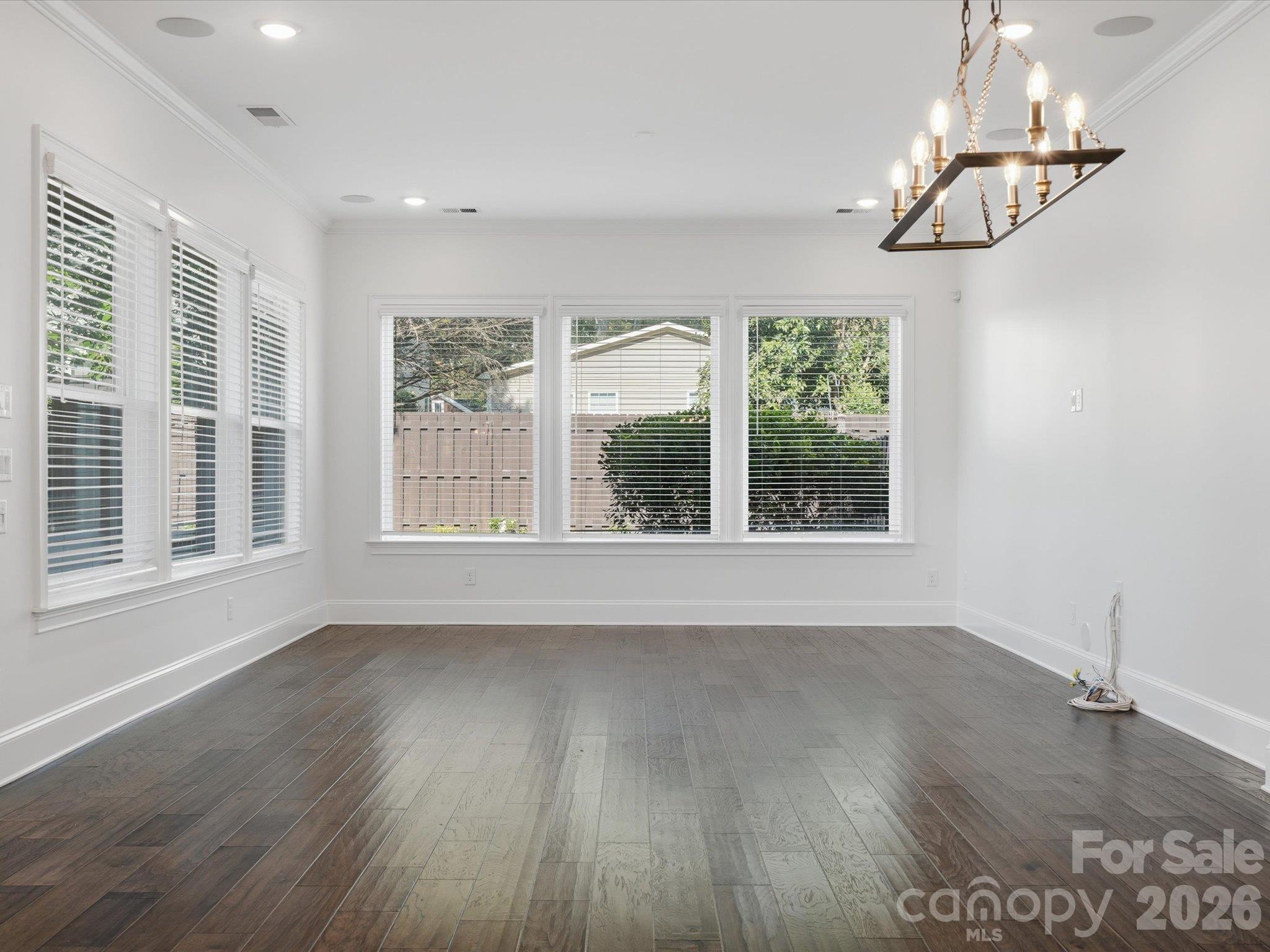 Dining area with modern linear chandelier, triple windows, crown molding, and LVP flooring, open to the kitchen and living room for easy entertaining. - 337 Belton Street, Charlotte