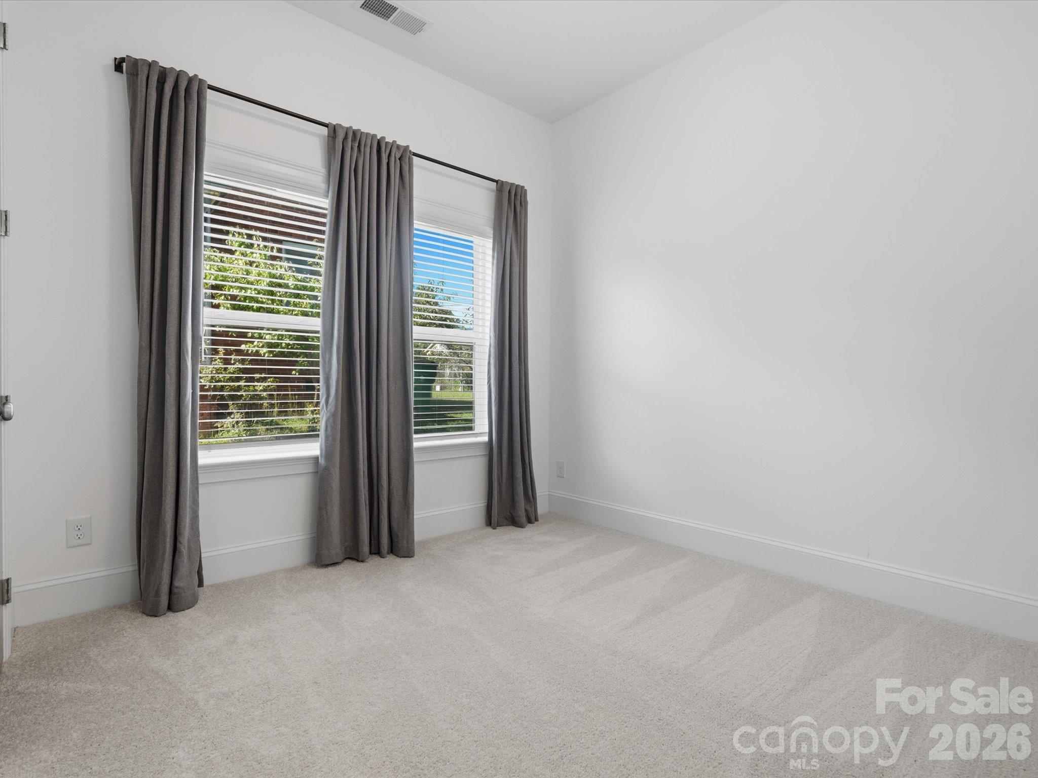 Main-level guest bedroom (Bedroom 1) with en suite bath, plush carpet, and large window. A first-floor guest suite that also works well as a home office. - 337 Belton Street, Charlotte