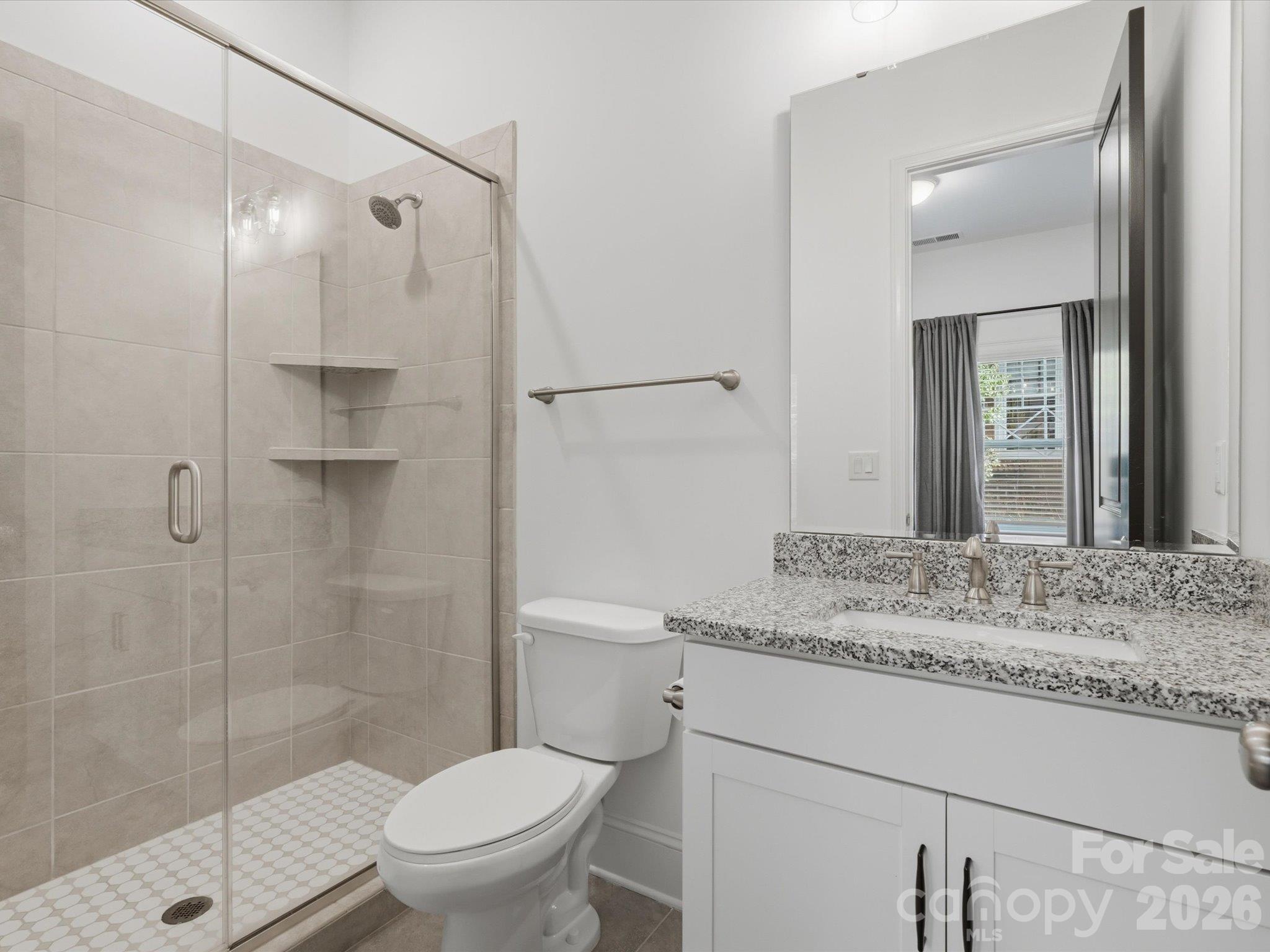 Main-level en suite bathroom with glass-enclosed walk-in shower, tile surround, granite-topped white vanity, and brushed nickel fixtures. - 337 Belton Street, Charlotte