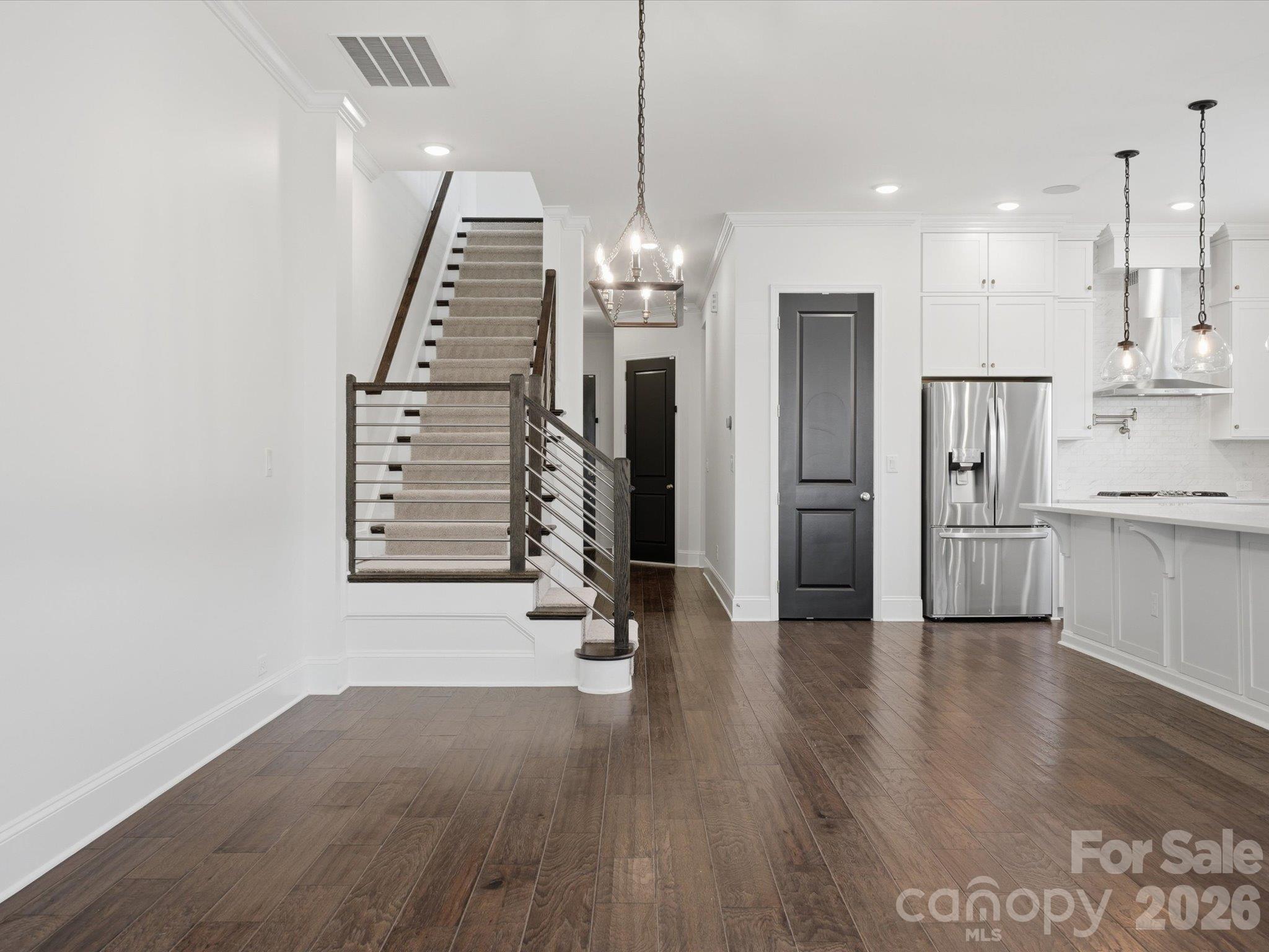 Modern staircase with horizontal metal railing and wood handrail, open to the kitchen and stainless French-door refrigerator on the main level. - 337 Belton Street, Charlotte