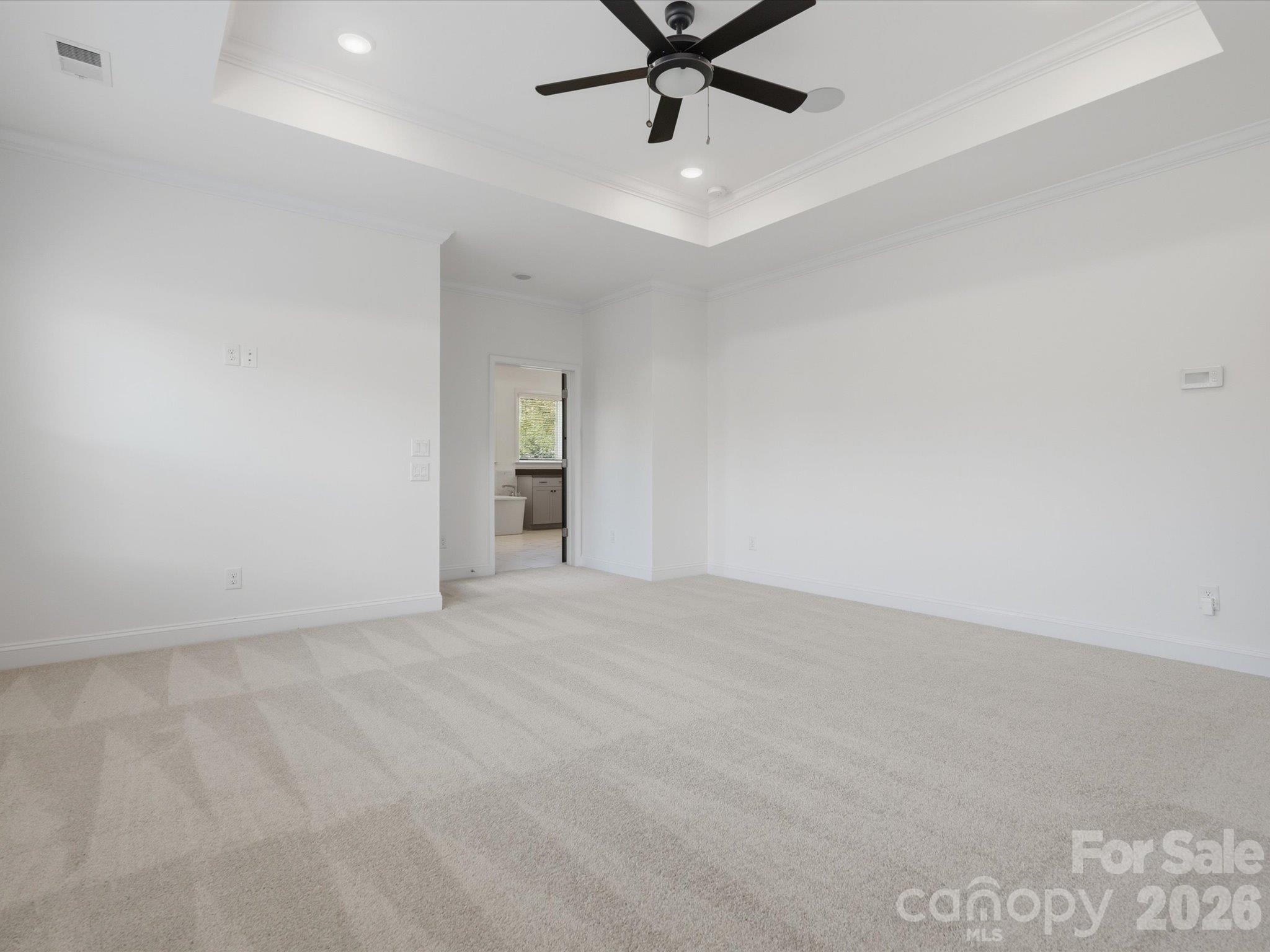 Expansive primary bedroom with tray ceiling and crown molding, showing the entry to the spa-inspired en suite bathroom and custom walk-in closet. - 337 Belton Street, Charlotte
