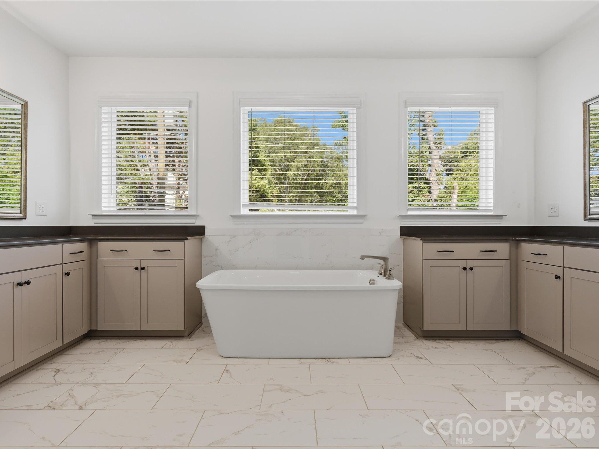 Spa-inspired primary bathroom with freestanding soaking tub centered between dual vanities, marble-look tile, and three windows for natural light. - 337 Belton Street, Charlotte