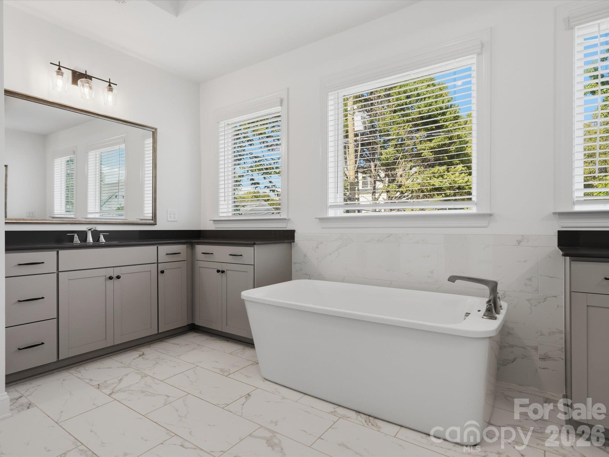 Freestanding soaking tub with tub filler, marble-look tile flooring, and separate vanities in the spa-style primary bathroom. - 337 Belton Street, Charlotte