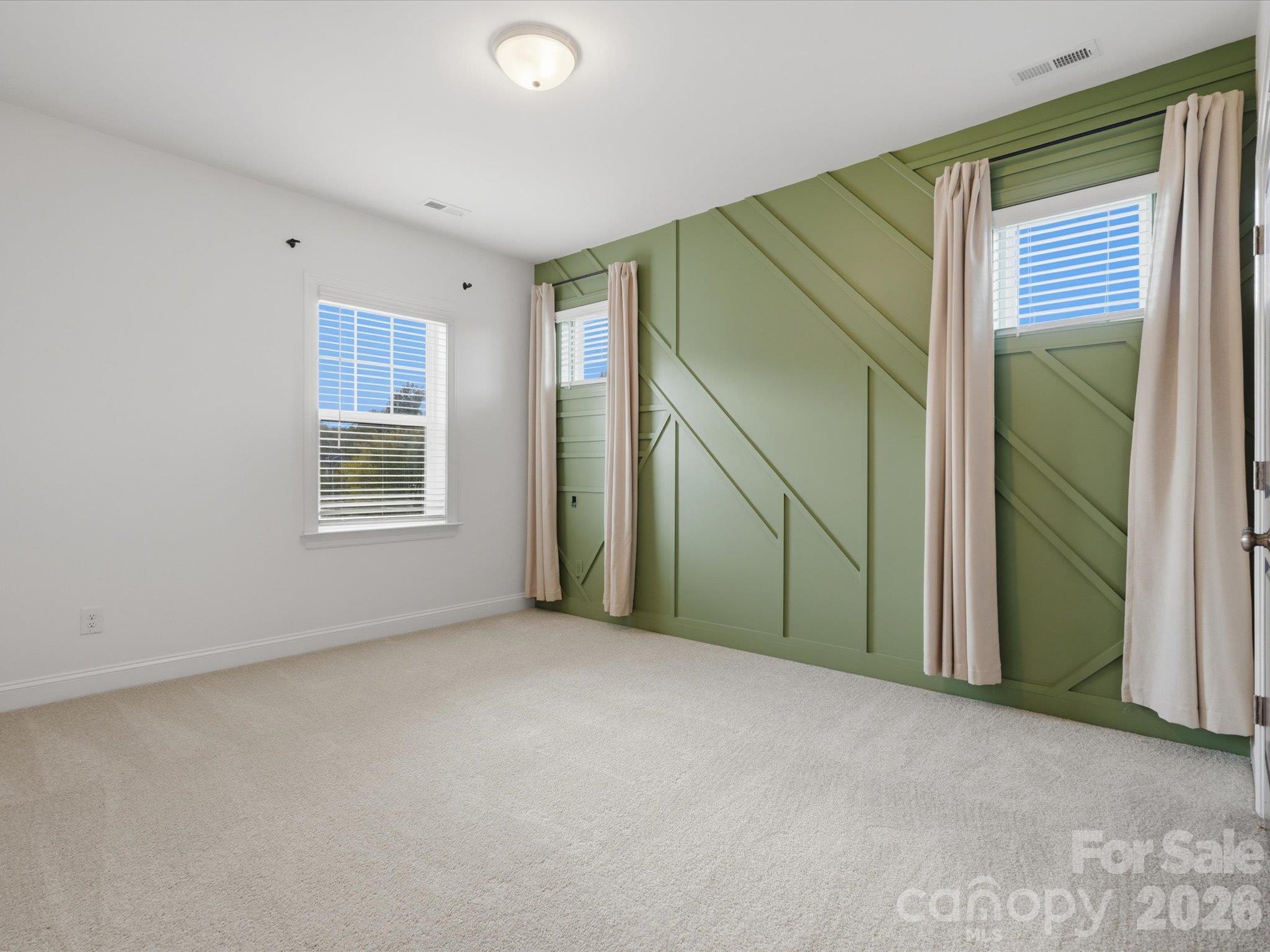 Upstairs second guest bedroom with custom sage green geometric accent wall, large windows, and plush carpet. - 337 Belton Street, Charlotte