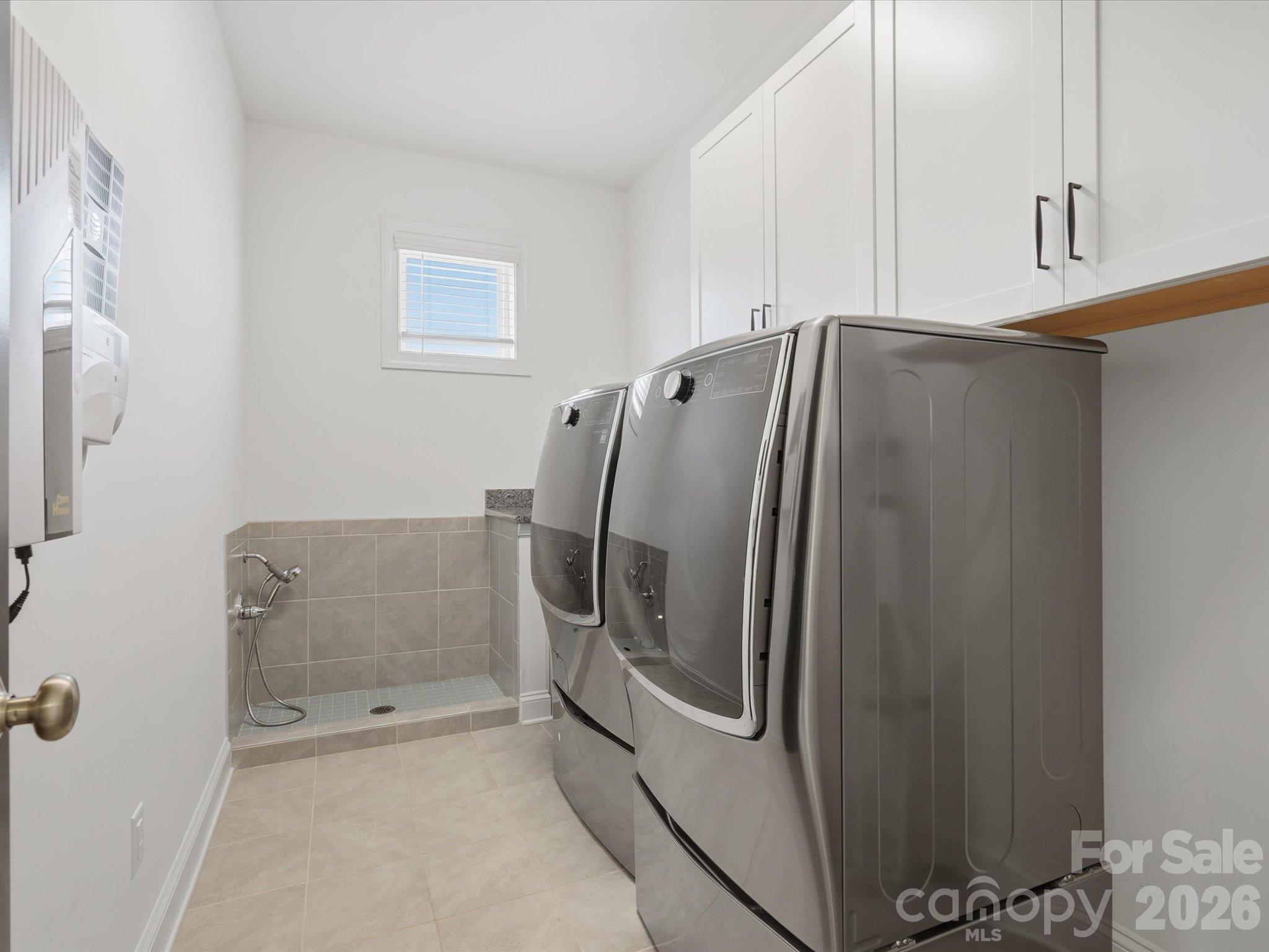 Second-floor laundry room with upper cabinetry, tile flooring, and built-in utility shower that works as a pet wash station. - 337 Belton Street, Charlotte