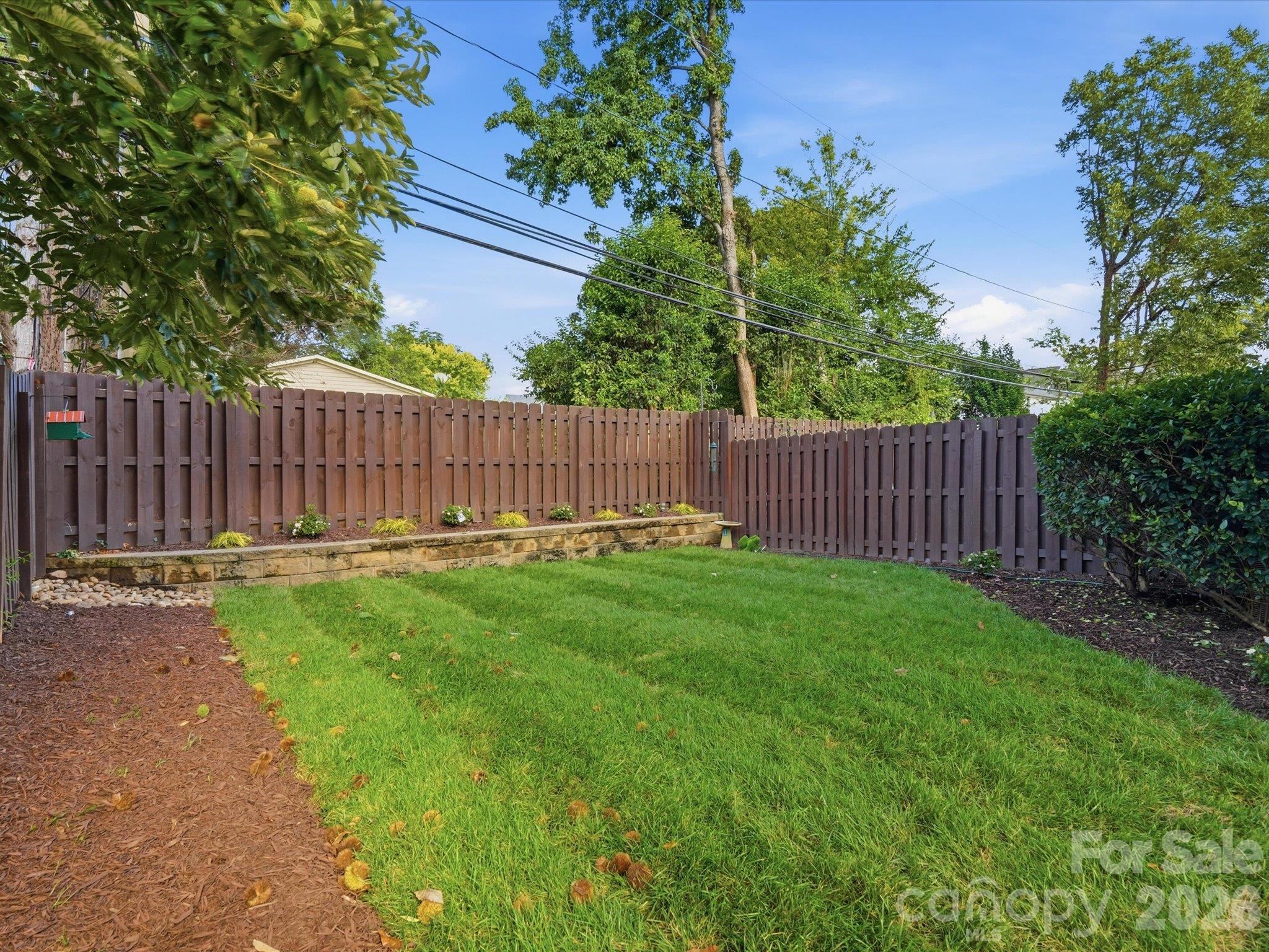 Level, fully fenced backyard with lush lawn, raised planting bed, and mature trees. Private green space rarely found in a South End area townhome. - 337 Belton Street, Charlotte