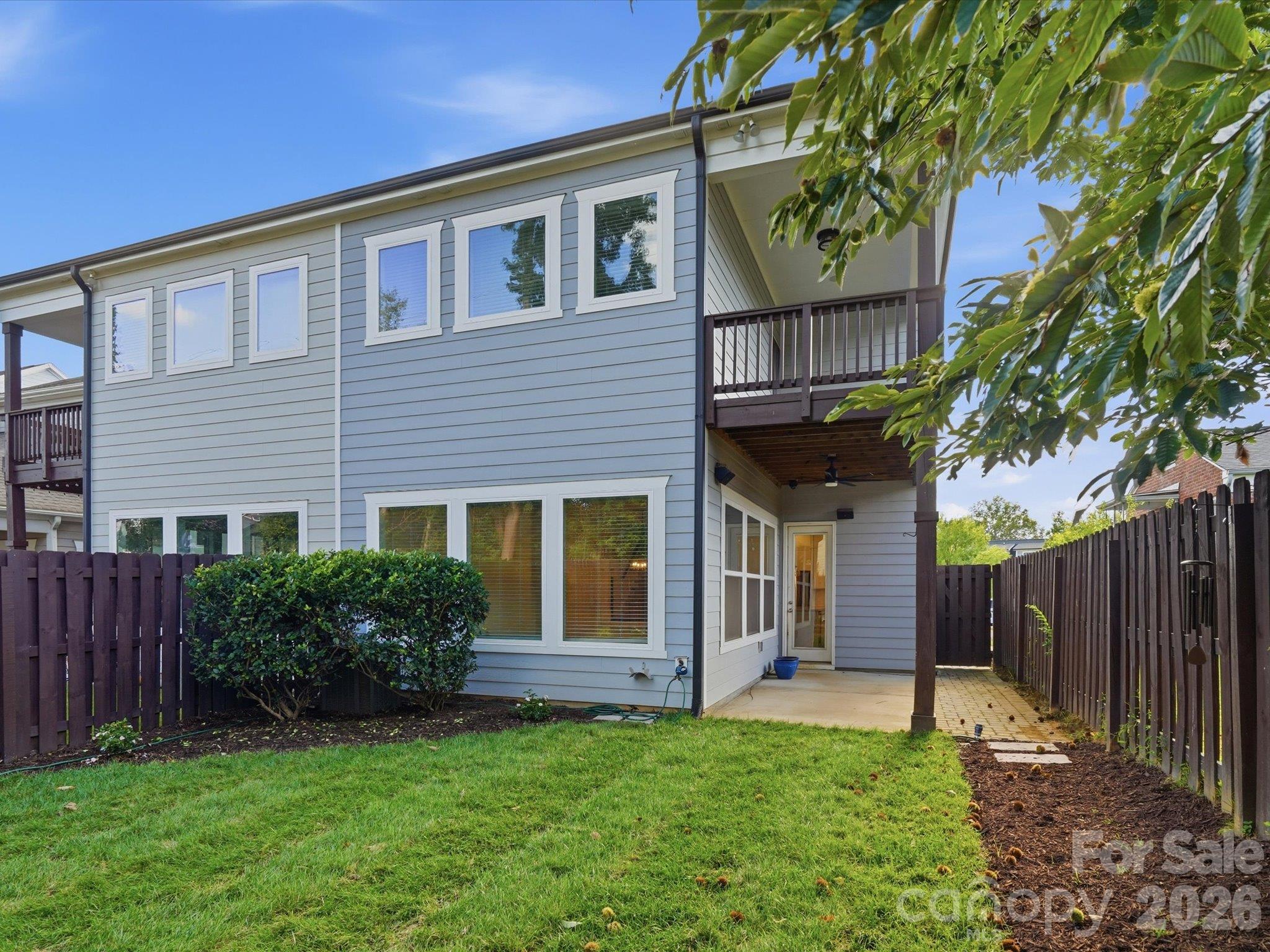 Rear exterior showing the covered patio, private primary suite deck, and lush fenced backyard of this Charlotte end-unit townhome. - 337 Belton Street, Charlotte