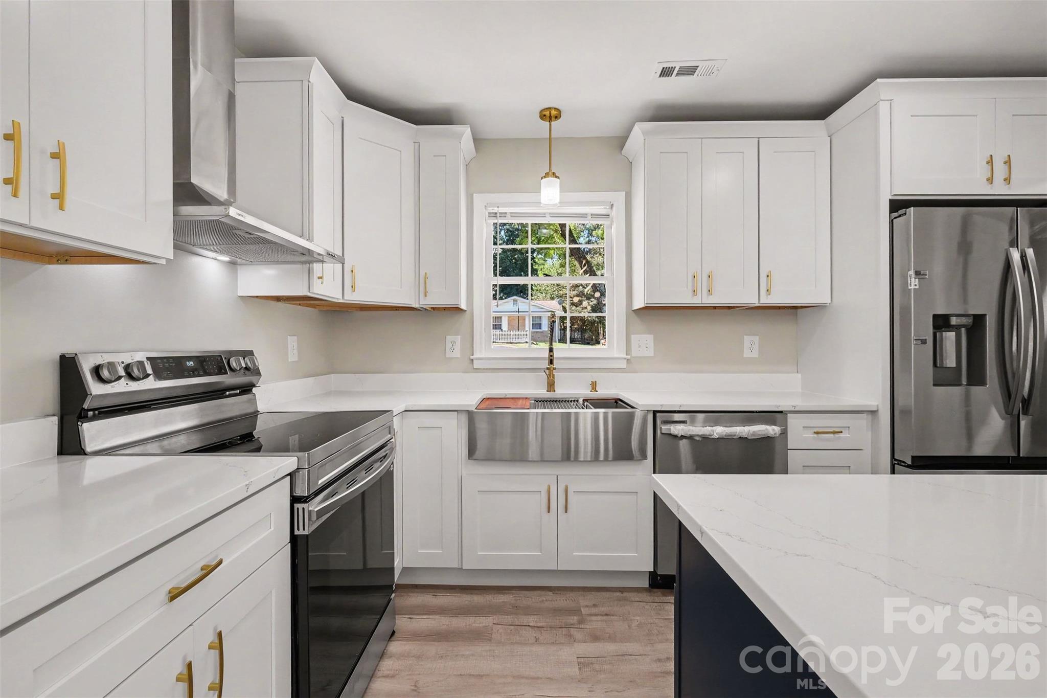 Renovated kitchen detail highlighting the stainless steel apron sink, premium range, and new white cabinetry with gold hardware. - 3801 Hillock Court, Charlotte
