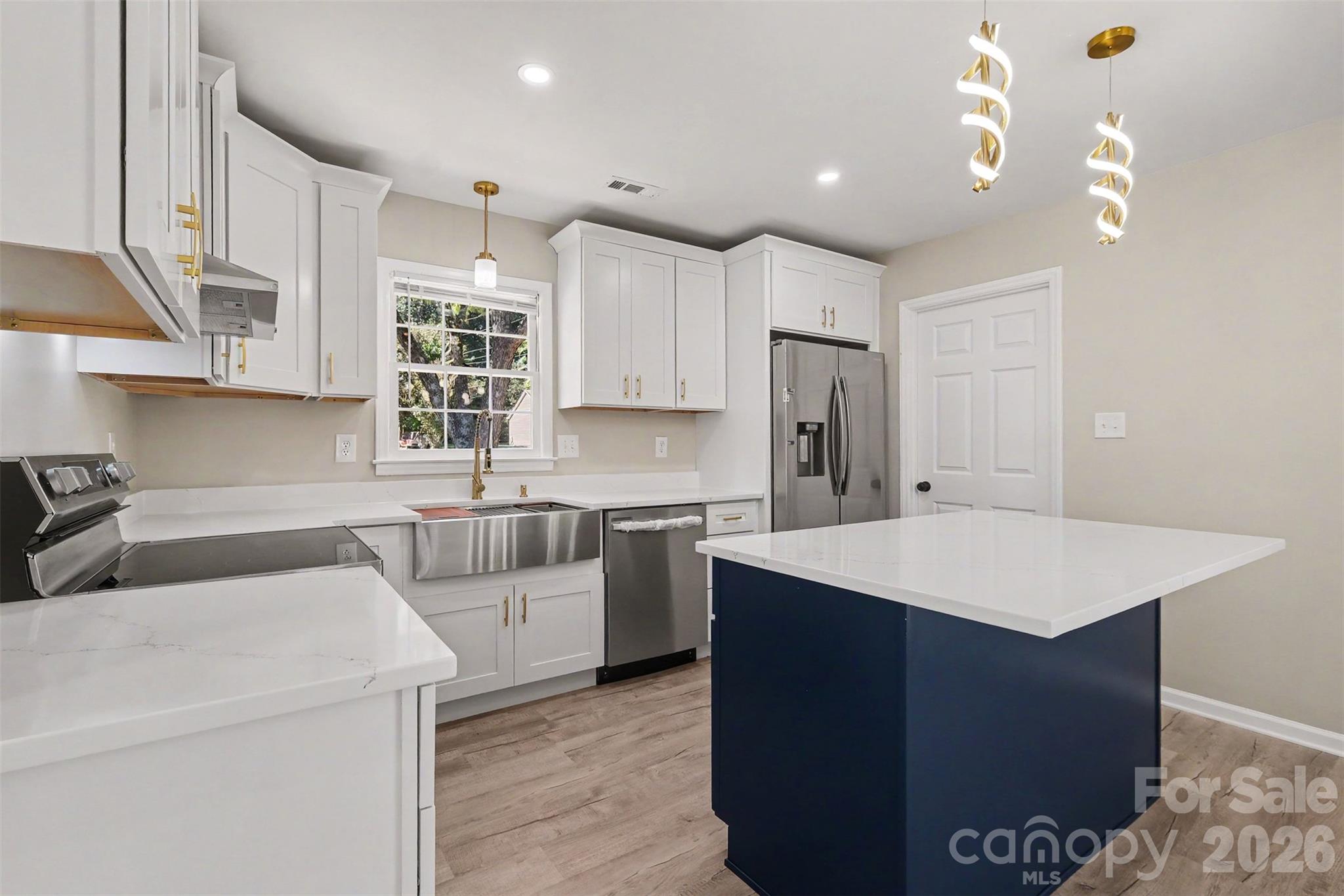 Renovated kitchen view highlighting the contrasting center island, stainless steel refrigerator, apron sink, and door leading to the dedicated laundry room. - 3801 Hillock Court, Charlotte