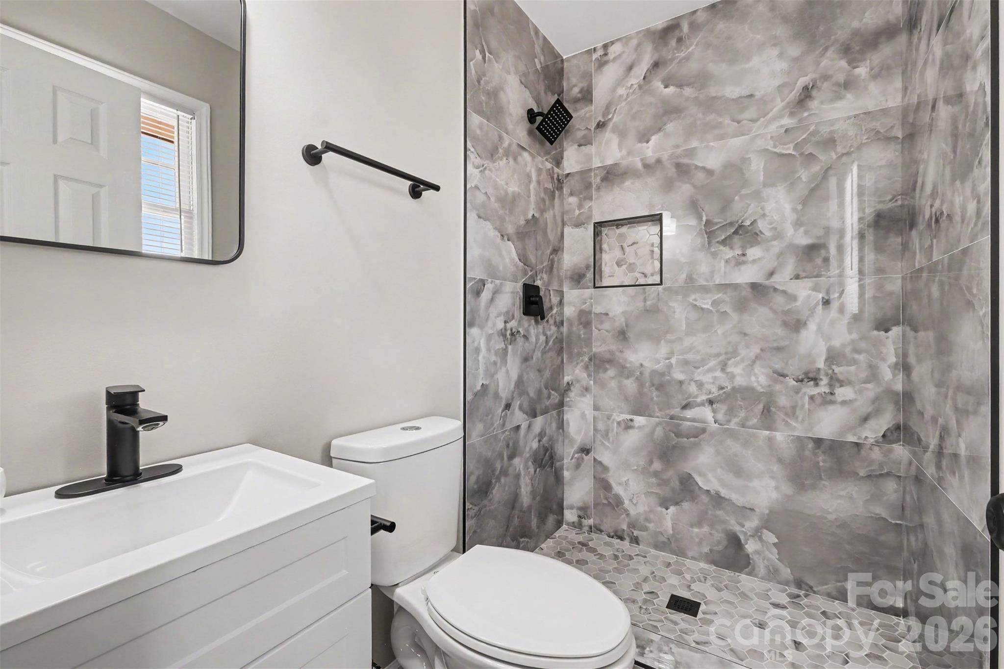 Luxurious primary ensuite featuring a custom walk-in shower with floor-to-ceiling dark porcelain tile, modern vanity, and sleek black fixtures. - 3801 Hillock Court, Charlotte