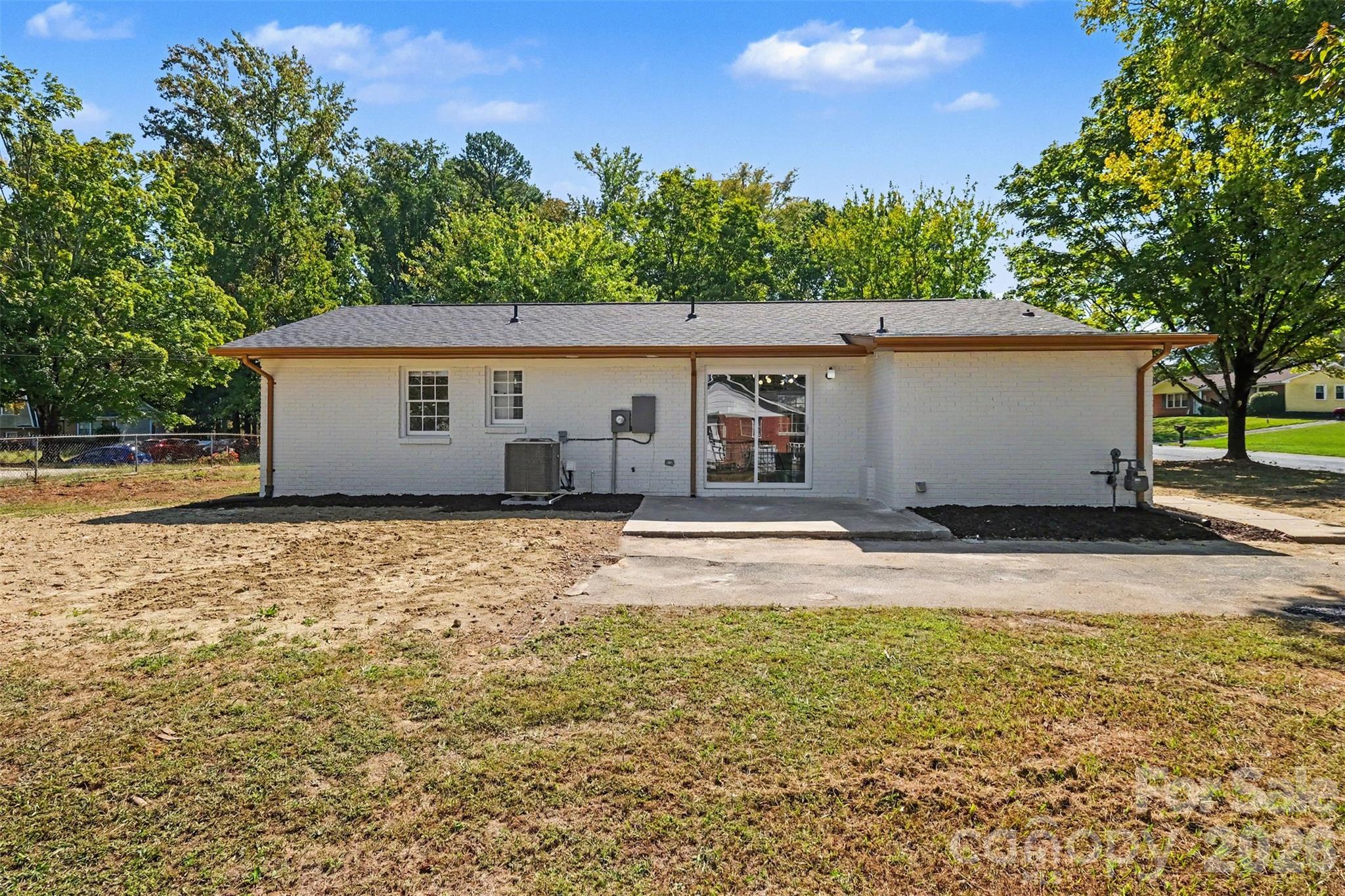 Rear exterior view showcasing the painted brick facade, concrete patio slab, sliding glass door entry, and expansive backyard. - 3801 Hillock Court, Charlotte