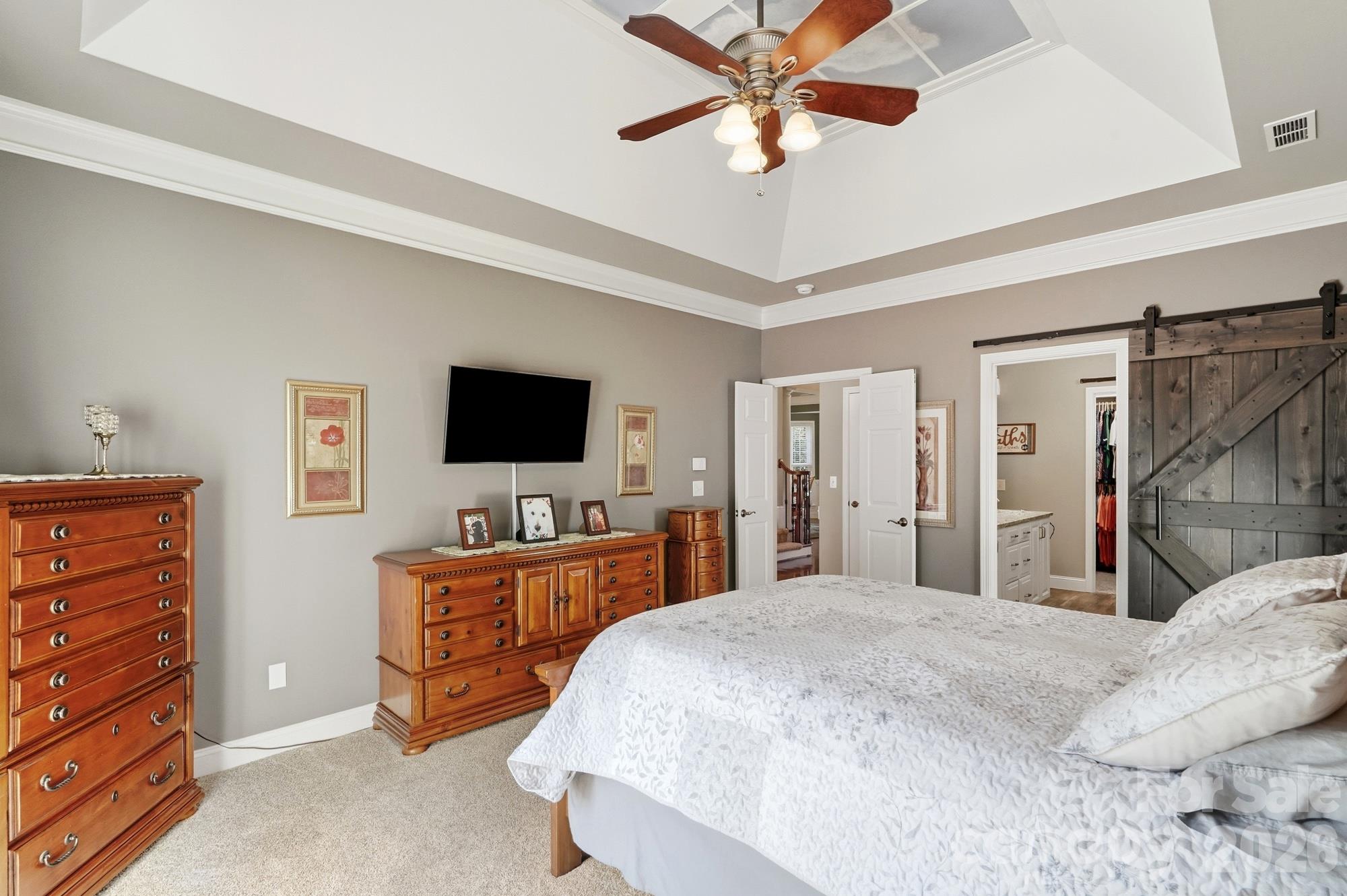 The primary bedroom is located on the main level and has a tray ceiling with accents that bring the outdoors indoors. The sliding barn door creates space that a door would ordinarily take up and gives access to the fully updated primary bathroom. - 120 Harris Farm Road, Mooresville