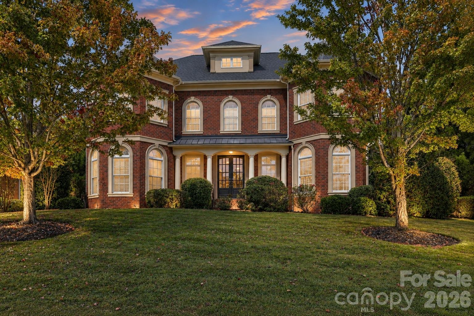 A striking evening view highlights this full-brick Weddington Chase home framed by mature trees and established landscaping. - 2309 Highland Forest Drive, Waxhaw
